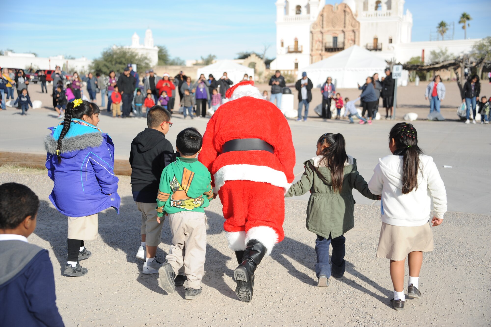 The youngest students at San Xavier Mission School escort Santa Claus during Davis-Monthan Air Force Base’s 50th Anniversary Santas in Blue event in Tucson, Ariz., Dec. 10, 2015. San Xavier Mission School provides education to nine grades starting with their pre-kindergarten to seventh grade. (U.S. Air Force photo by Airman 1st Class Ashley N. Steffen/Released)