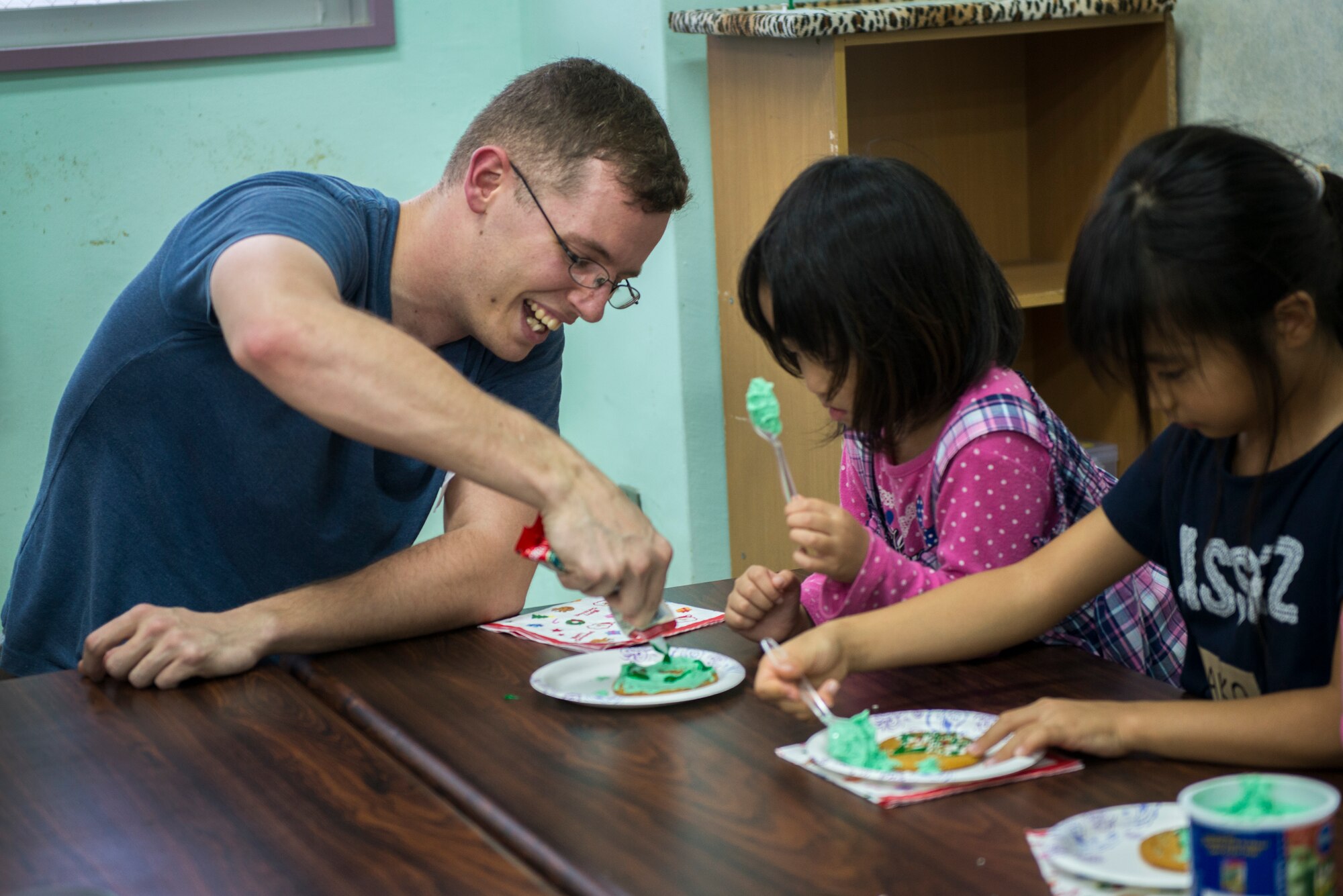 U.S. Air Force Staff Sgt. Damon Schmidt, 18th Communications Squadron cyber transport supervisor, helps a child decorate a Christmas cookie at the Midori School-Age Program during a volunteer visit, Dec. 10, 2015, in Okinawa City, Japan. Frequent interaction with the local community bolsters ties between the U.S. military and its host nation partners. (U.S. Air Force photo by Staff Sgt. Maeson L. Elleman)