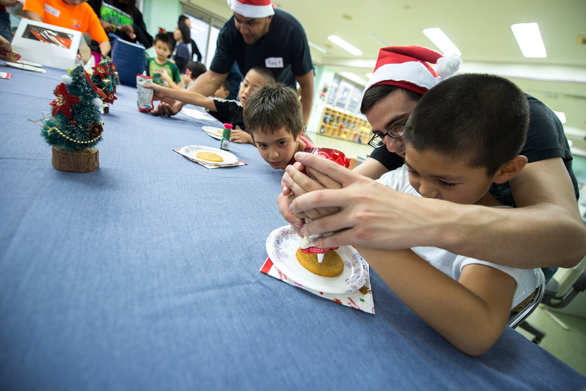 U.S. Air Force Senior Airman Thomas Baebler, 18th Communications Squadron radio frequency transmissions technician, helps a child decorate a Christmas cookie at the Midori School-Age Program during a volunteer visit, Dec. 10, 2015, in Okinawa City, Japan. The visit gave 14 American volunteers the opportunity to share Christmas customs with the local community and improve local relationships. (U.S. Air Force photo by Staff Sgt. Maeson L. Elleman)