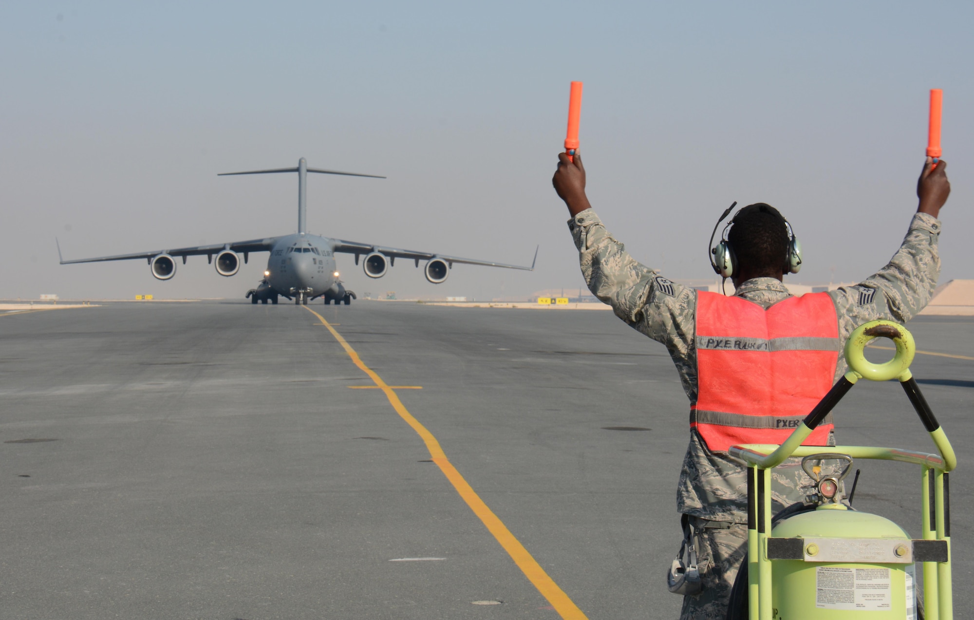 Staff Sgt. Berry Lynch, 8th Expeditionary Air Mobility Squadron avionics specialist, directs a C-17 Globemaster III to its parking location at Al Udeid Air Base, Qatar Dec. 13. The aircraft delivered two Apache helicopters from Fort Bliss, Texas. The helicopters are scheduled to take part in the annual Qatar National Day Parade set for Dec. 18. (U.S. Air Force photo by Tech. Sgt. James Hodgman/Released)