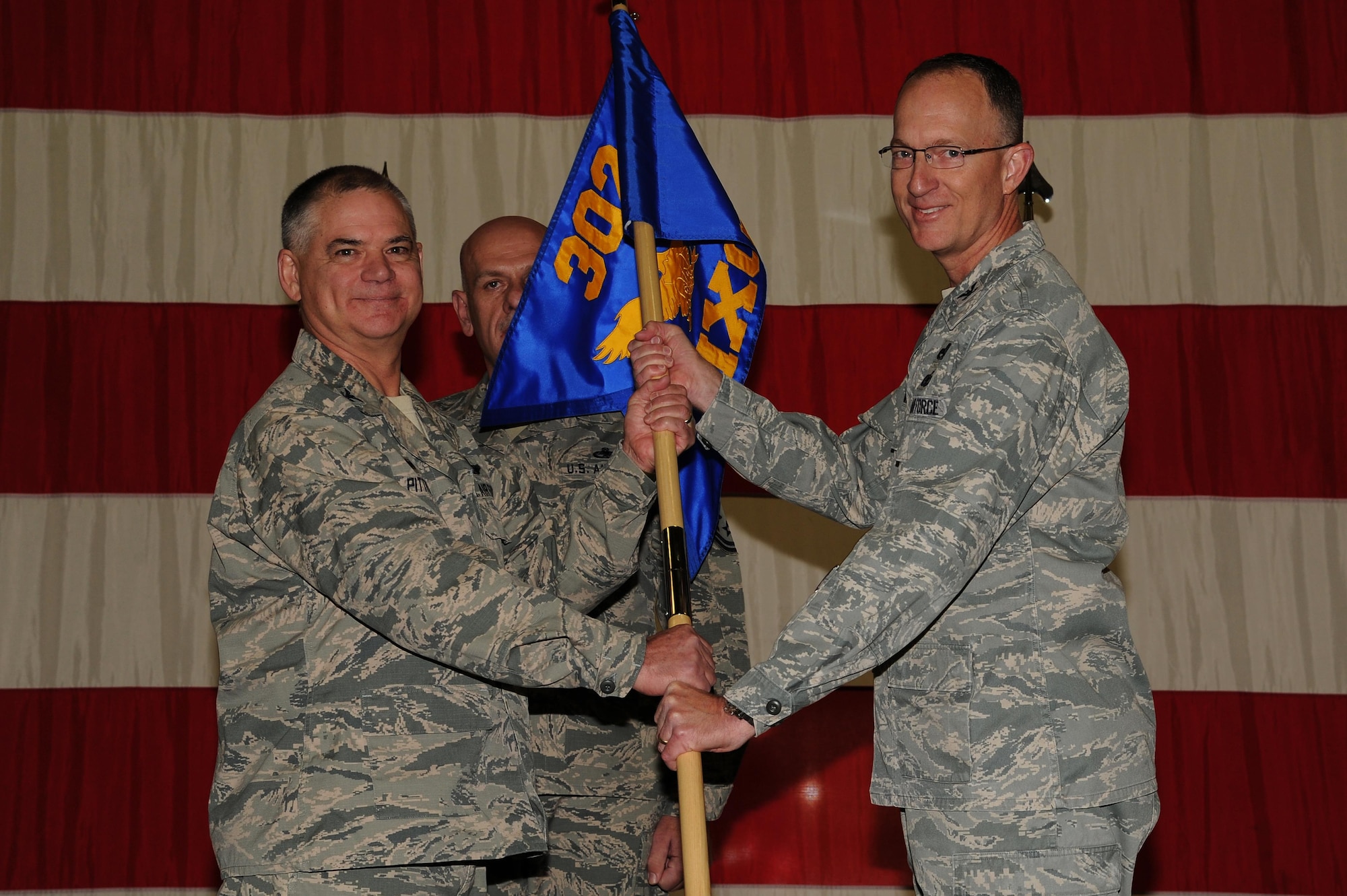 Col. Jack H. Pittman Jr., left, 302nd Airlift Wing commander, passes the 302nd Maintenance Group guideon to Col. Jeffrey Higgins during an assumption of command ceremony Dec. 5, 2015 here. Before assuming command of the Peterson-based Reserve wing’s maintenance group, Higgins was an Individual Mobilization Augmentee, assigned to Headquarters Air Force, directorate of logistics, nuclear weapons missiles and munitions division at the Pentagon, Washington, D. C. Higgins is taking over the 302nd MXG just after the 302nd AW was recognized by the Airlift Tanker Association by being named the Lt. Gen. James E. Sherrard III award winner. Among many of the Reserve wing’s notable achievements, the award commends the efforts of the 302nd Aircraft Maintenance Squadron for producing four out of the five top performing C-130s in the Air Force Reserve Command. Higgins served as the deputy commander of the 302nd MXG from October 2007 to September 2009. He is familiar with the wing and has a goal for the group. During the ceremony Higgins characterized perseverance and passion for long-term goals as “grit.” He stated, “We already have a lot of grit in the 302nd maintenance group, it’s what allows us to turn an airplane to make another line, it drives us to return an aircraft to mission capable status and not cut corners. It pushes us to take care of our people while taking care of our mission. My goal is for us to be the grittiest maintenance group in this [Air Force Reserve] command.”  (U.S. Air Force photo/Senior Airman Amber Sorsek)