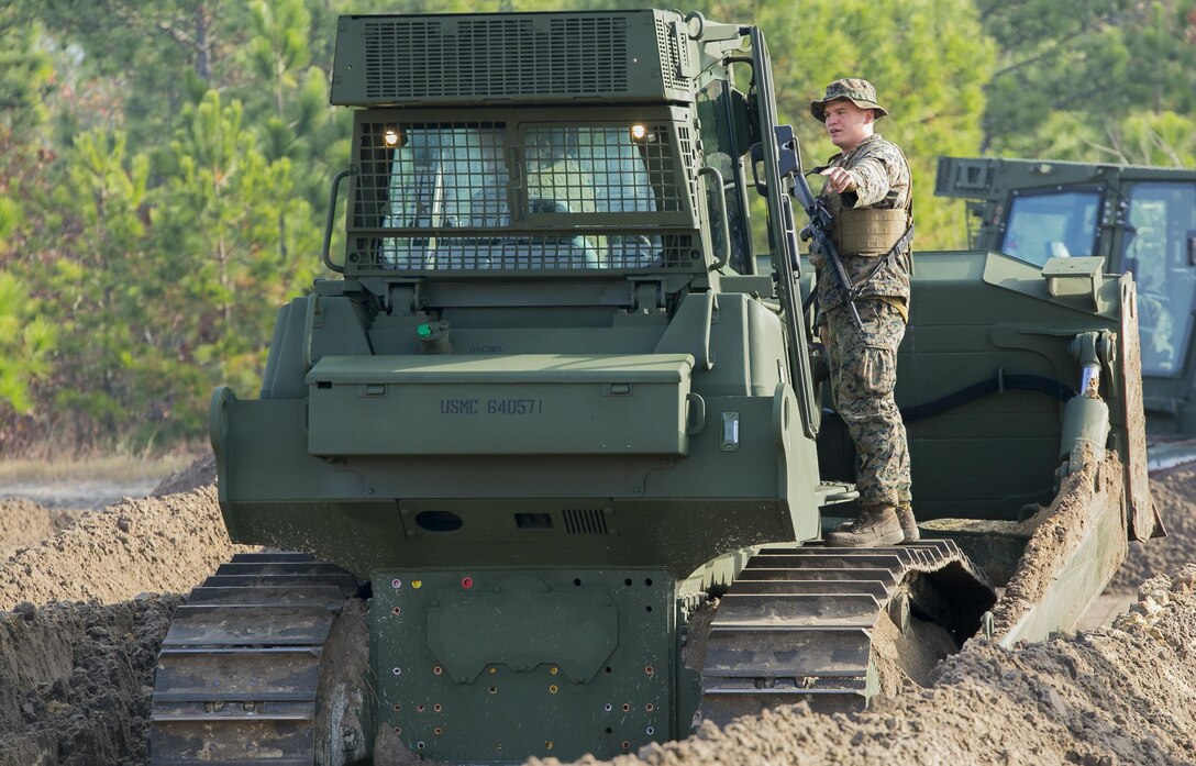 A heavy equipment operator with Combat Logistics Battalion 6, 2nd Marine Logistics Group directs a Medium Crawler Tractor during a development of a simulated Forward Operating Base exercise at Camp Lejeune, N.C., Dec. 8, 2015. “This is a good learning experience for our battalion,” Lance Cpl. Taylor Woolman, a heavy equipment operator with CLB 6 said. “Our operators don’t always have the opportunity to use this heavy equipment especially while the unit is in garrison.”  The operators within the unit prepare for future operations by conducting training parallel to what they would be doing in a deployed environment. (U.S. Marine Corps photo by Lance Cpl. Luke J. Hoogendam/Released)