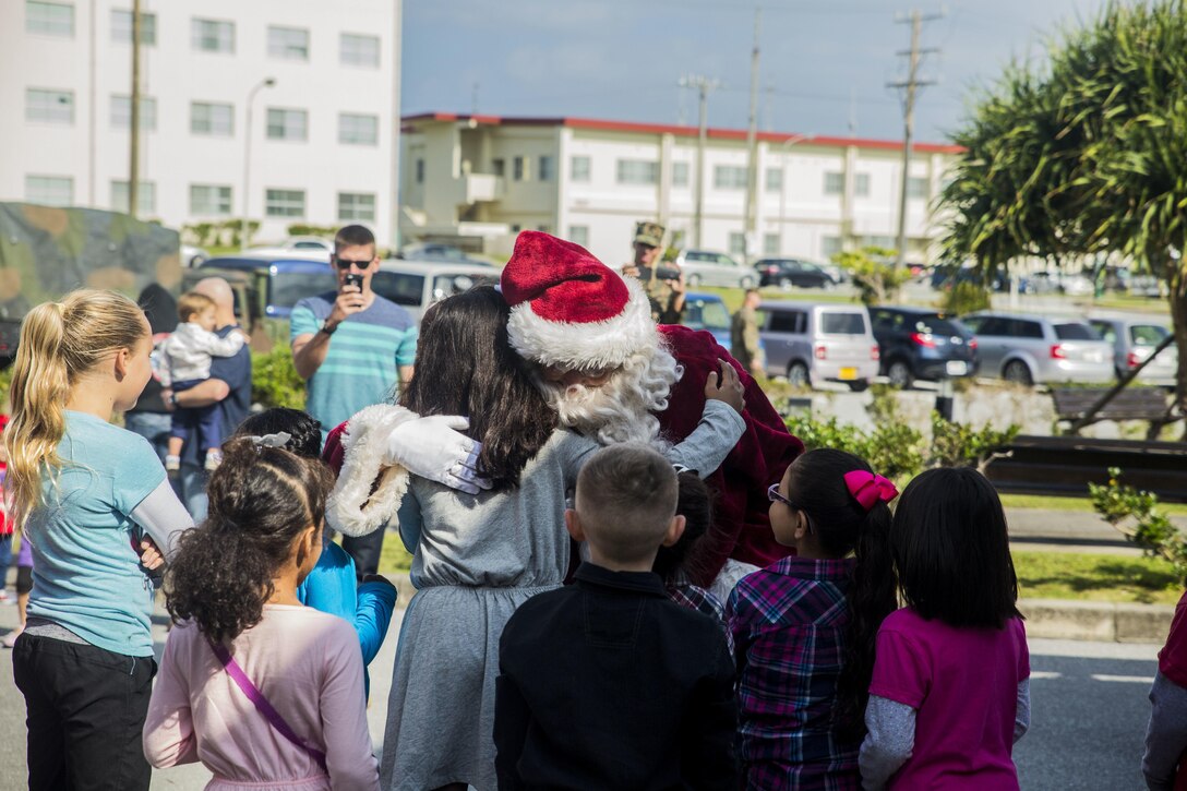 Santa Claus hugs children when he arrives for the event, Santa’s Little Helper, on Camp Hansen, Okinawa, Japan, Dec. 12, 2015. The event also had Santa fast rope out of a helicopter, fake snow, a bouncy castle, face painting and food served. The event was hosted by Combat Assault Battalion, 3rd Marine Division, III Marine Expeditionary Force and Marine Corps Community Services. (U.S. Marine Corps photo by Cpl. Tyler S. Giguere/Released)