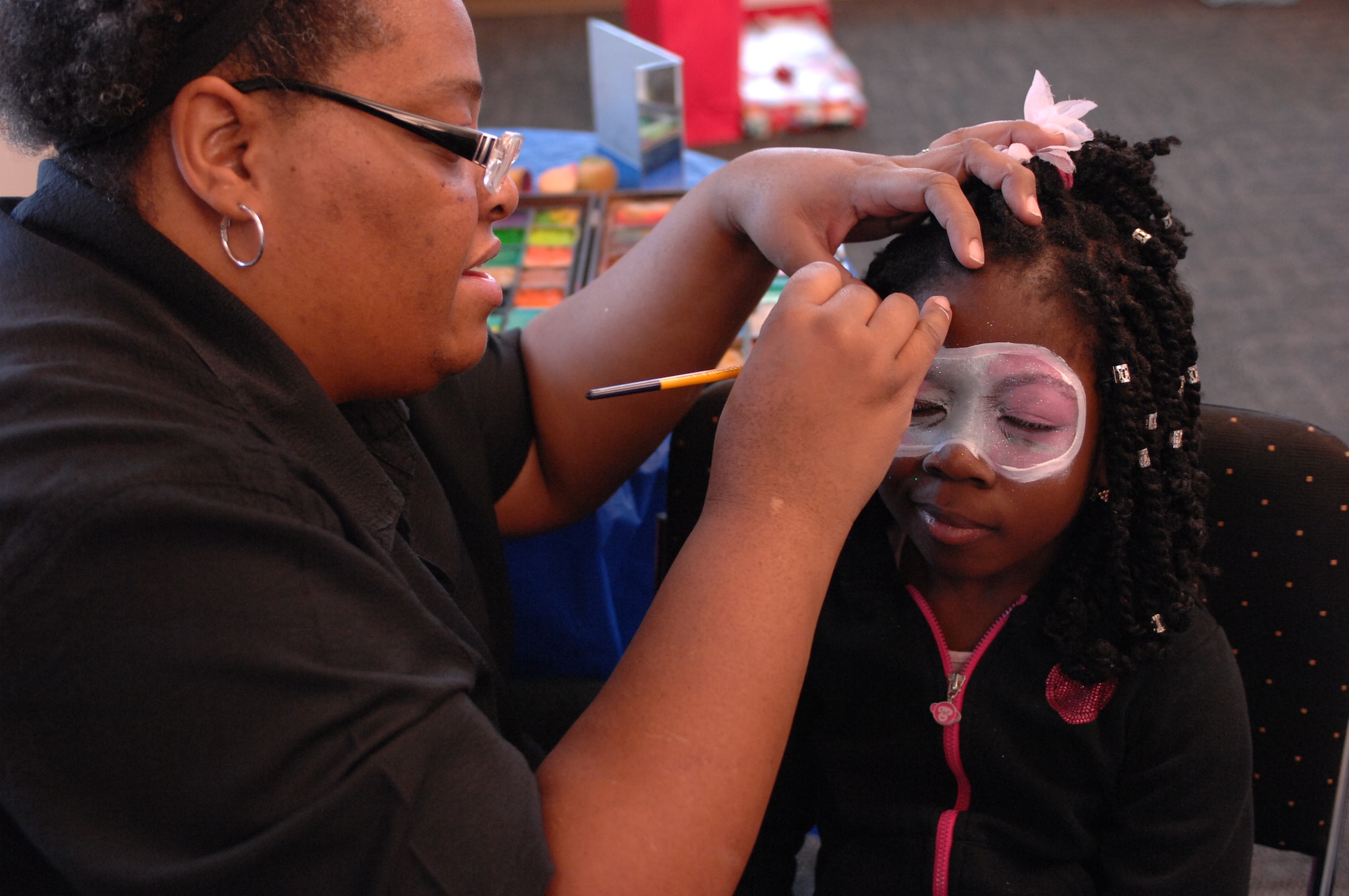 A child attending a holiday party sponsored by the Reconnaissance Crews Booster Club squints as her face is painted at the Pointe at Rising View, Offutt Air Force Base, Neb., Dec. 12, 2015. The event combined a holiday party with a shopping trip in which underprivileged children received money to spend on winter clothing and shoes. (U.S. Air Force photo/Senior Airman Rachel Hammes)