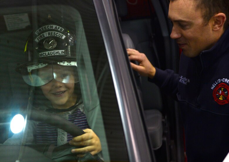Hunter, son of Staff Sgt. Keith, 30th Reconnaissance Squadron NCO in charge of plans and projects, sits at the wheel of a fire truck with Landon, 99th Civil Engineer Squadron firefighter, during the Children's Holiday Party Dec. 12, 2015, at Creech Air Force Base, Nevada. The event included many activities to bring Creech families together, improve morale, and camaraderie, as well as, provide opportunities for children to meet Santa and win presents. (U.S. Air Force photo by Airman 1st Class Christian Clausen/Released)