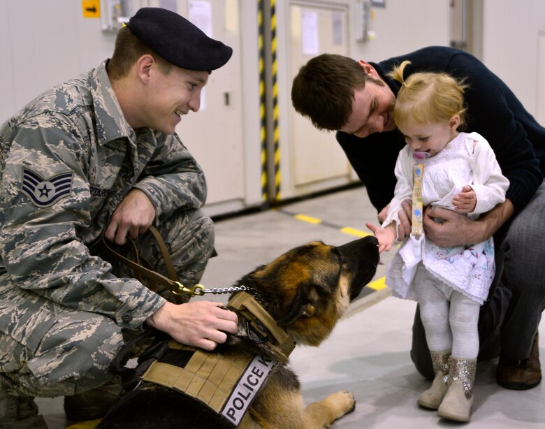 Military Working Dog Dakrosy licks Mia, 1, daughter of a 42nd Attack Squadron member, during the third annual Children's Holiday Party Dec. 12, 2015, at Creech Air Force Base, Nevada. The event brought soon to be retired MWD for an opportunity for kids to pet him in order to transition him from working dog to a civilian atmosphere. (U.S. Air Force photo by Airman 1st Class Christian Clausen/Released))