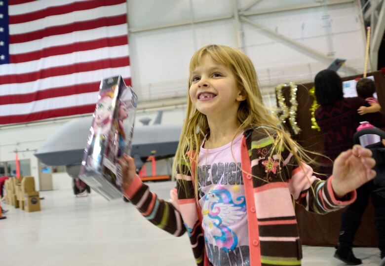 Lillian, 7, daughter of Master Sgt. Jessica, 432nd Operations Support Squadron intelligence superintendent, jumps for joy after receiving a free Christmas present during the third annual Children's Holiday Party Dec. 12, 2015, at Creech Air Force Base, Nevada. She said her favorite parts of the day were playing games and meeting Santa. (U.S. Air Force photo by Airman 1st Class Christian Clausen/Released)