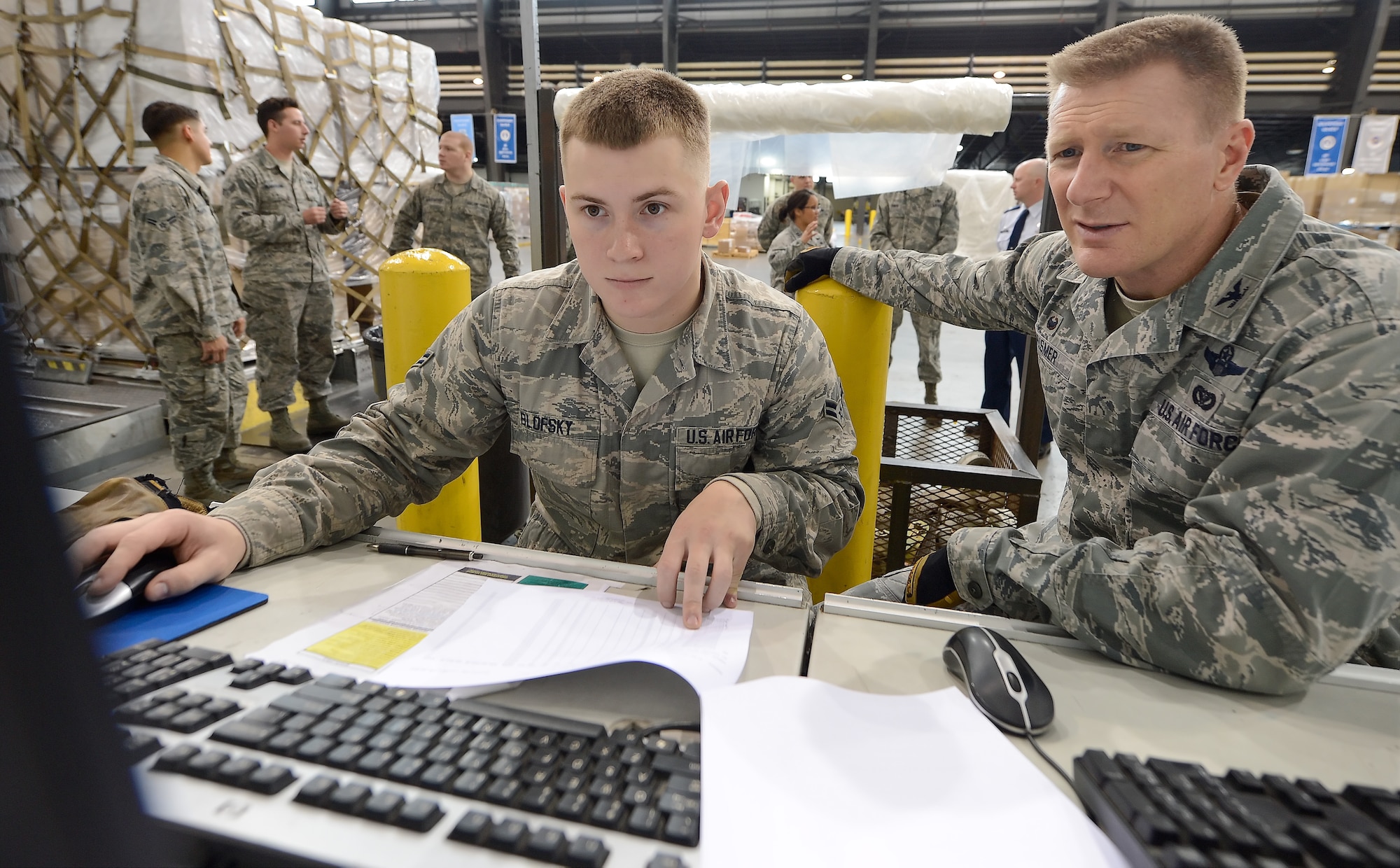 Airman 1st Class Tanner Blofsky, 436th Aerial Port Squadron cargo processor, works with Col. Michael Grismer, 436th Airlift Wing commander, during Grismer's visit to the 436th APS to learn how cargo is processed for aerial transport Dec. 10, 2015, at Dover Air Force Base, Del. Blofsky matches information from a paper listing to that in the computer before selecting the cargo for palletization. (U.S. Air Force photo/Greg L. Davis) 