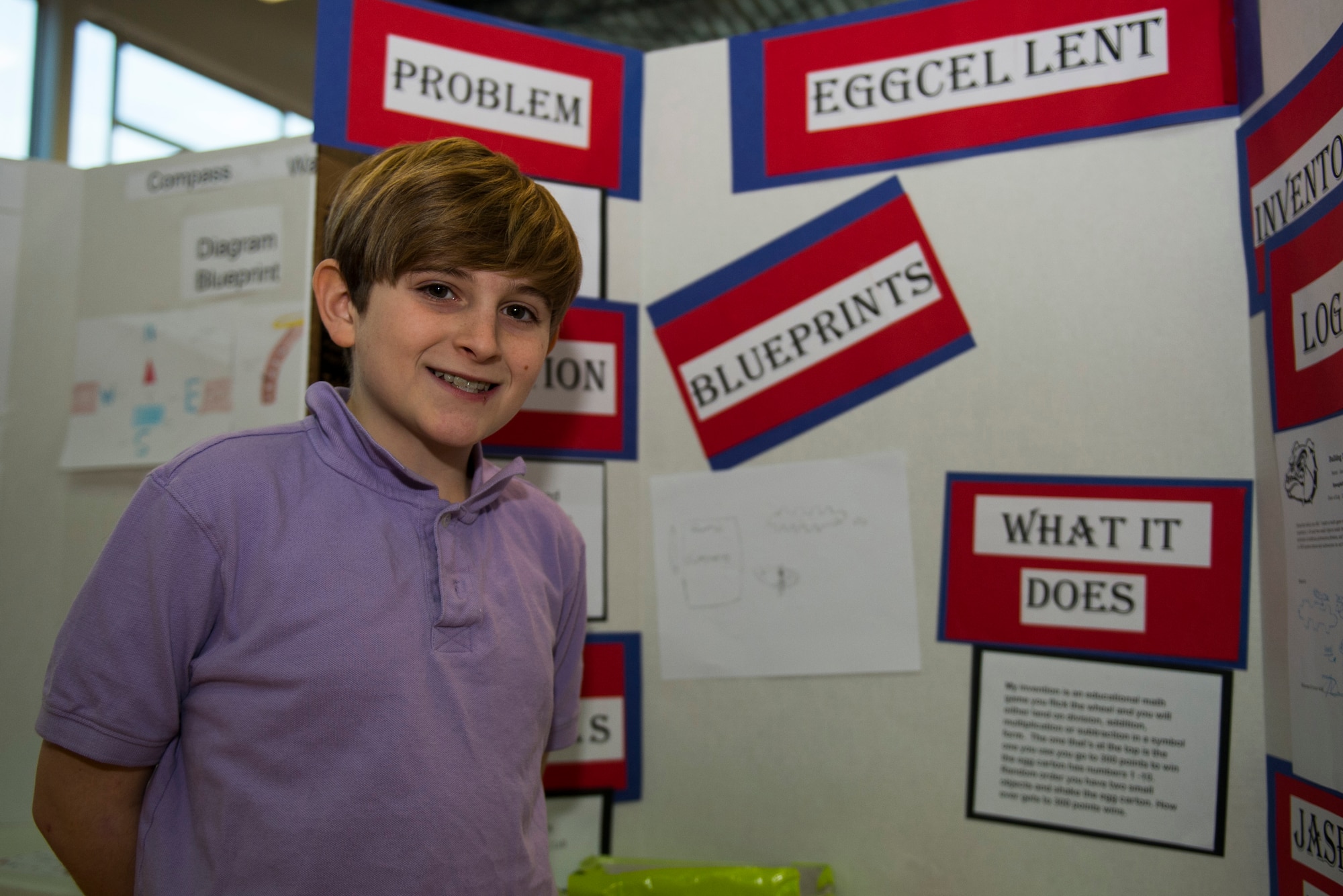 Jasper, a fifth grade student at Spangdahlem Middle High School, stands in front of his display board during the Invention Convention at Spangdahlem Air Base, Germany, Dec. 15, 2015. Jasper invented a game designed to enhance students’ math skills. (U.S. Air Force photo by Airman 1st Class Luke Kitterman/Released)