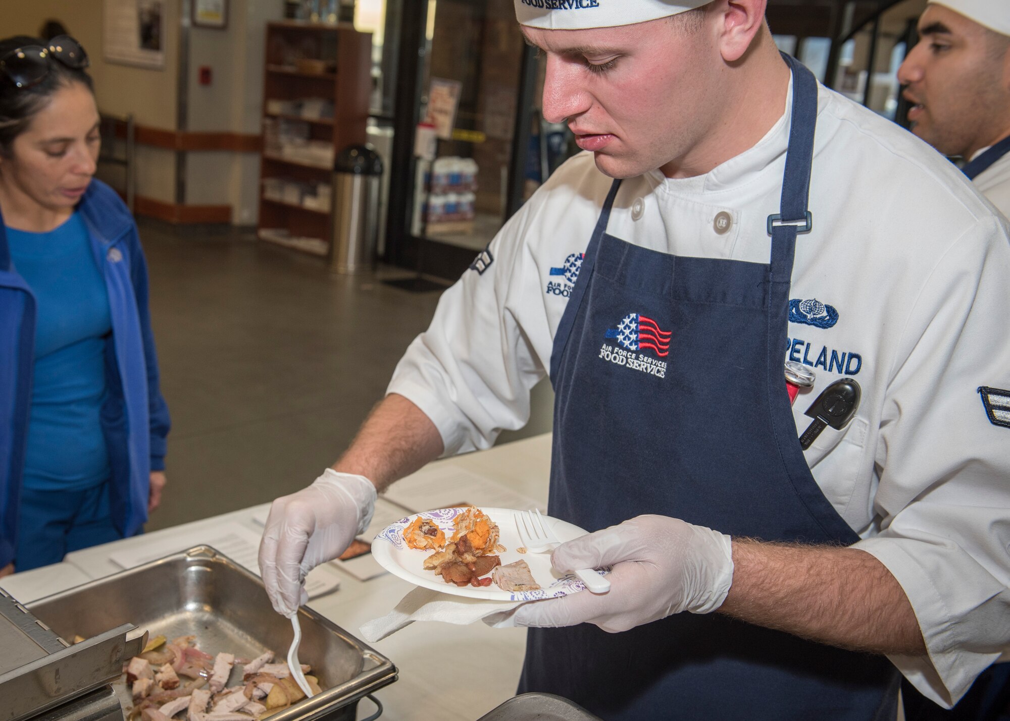 PETERSON AIR FORCE BASE, Colo. – Airman 1st Class Brandon Copeland, 21st Force Support Squadron dining facility journeyman, puts samples on a plate for a commissary customer during the Peterson Air Force Base Commissary Food Demo, Dec. 9, 2015. The Peterson Health and Wellness Center provided three healthy recipe options that can be cooked with common commissary products, which the Aragon Dining Facility chefs prepared and distributed to passersby’s at the commissary. (U.S. Air Force photo by Senior Airman Rose Gudex)