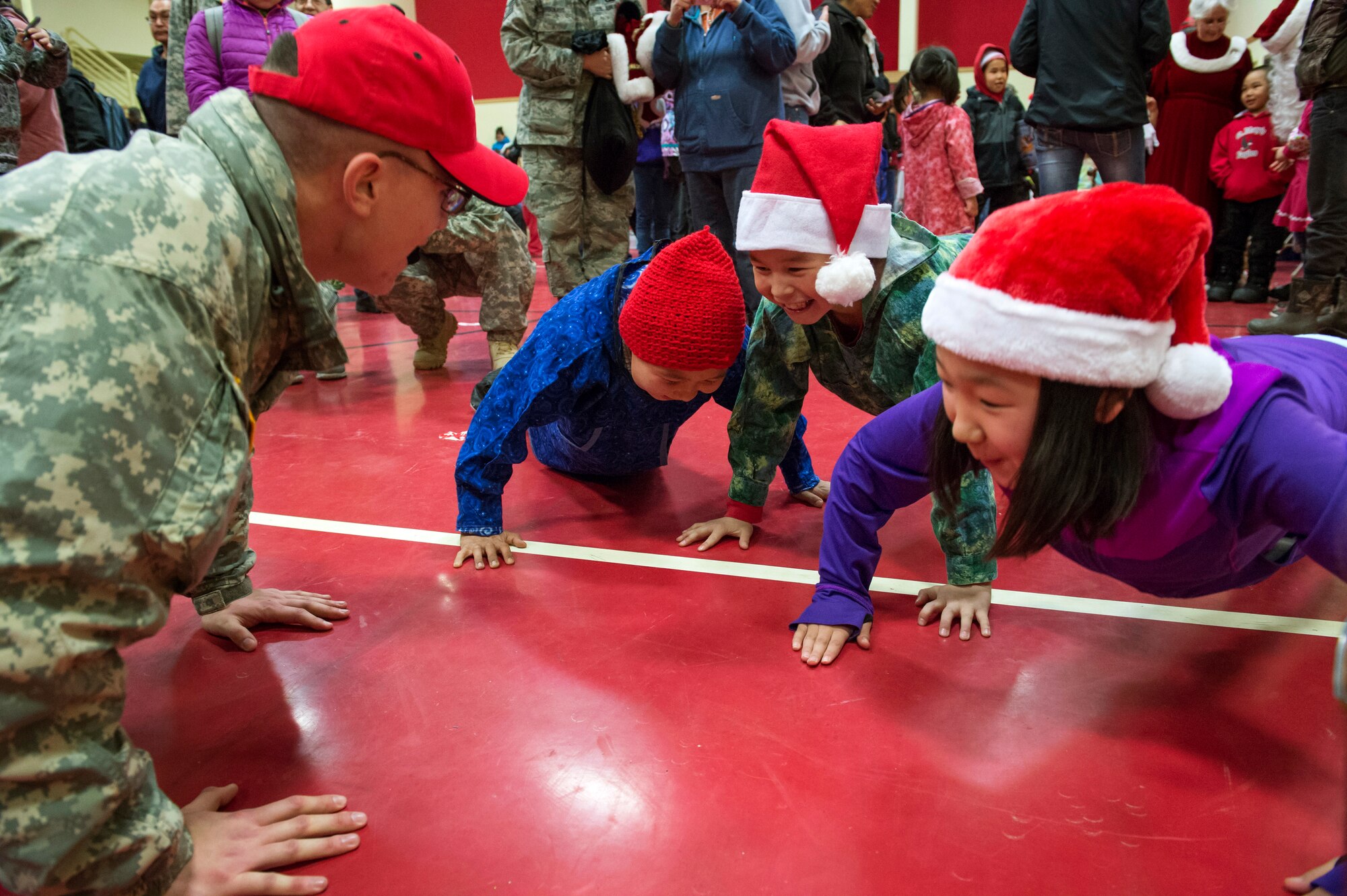 Alaska Army National Guard Spc. Michael Notti does pushups with elementary school children at St. Mary's, Alaska, during Operation Santa Claus, Dec. 5, 2015. This year marks the 59th year of the program, during which volunteers from approximately 30 groups and organizations came together to bring holiday cheer to underserved, remote communities across Alaska. (U.S. Air Force photo/Alejandro Pena)