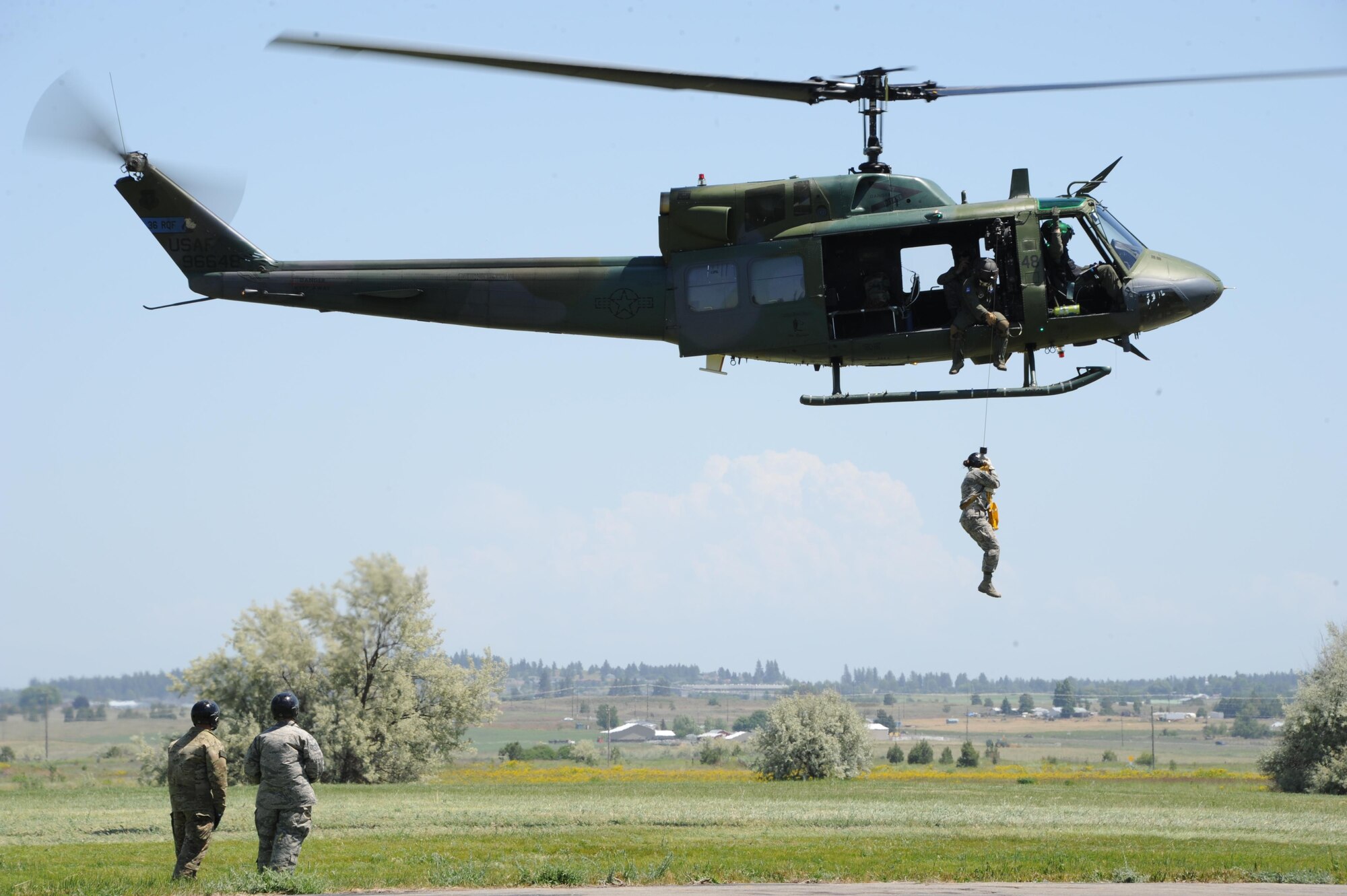 A Survival, Evasion, Resistance and Escape specialist and a combat survival student watch as another student is hoisted into the UH-1N Iroquois helicopter, June 10, 2015, at Fairchild Air Force Base, Wash. Students receive hands-on training with recovery devices while attending the Survival School. (U.S. Air Force photo/Airman 1st Class Nick J. Daniello)