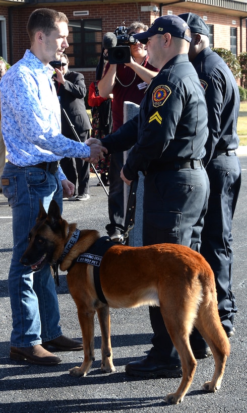 Former Marine Corps handler, David Pond (left), receives Pablo, a former military working dog, with Marine Corps Logistics Base Albany’s Marine Corps Police Department, from civilian police officer, Cpl. Greg Madrid, military working dog handler, MCPD, during an adoption ceremony held here, Dec. 15.