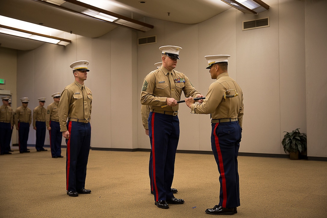 Sgt. Maj. Kent Cartmill (center), the outgoing senior enlisted leader of Marine Corps Recruiting Station Seattle, returns the sword of office to Maj. Sung Kim, his commanding officer, during a passage of command ceremony in Seattle Dec. 12, 2015. During the ceremony, Cartmill, from Garden City, Kan., was awarded a Meritorious Service Medal and relinquished duties to Sgt. Maj. Jeffrey Dagenhart. (U.S. Marine Corps photo by Sgt. Reece Lodder)