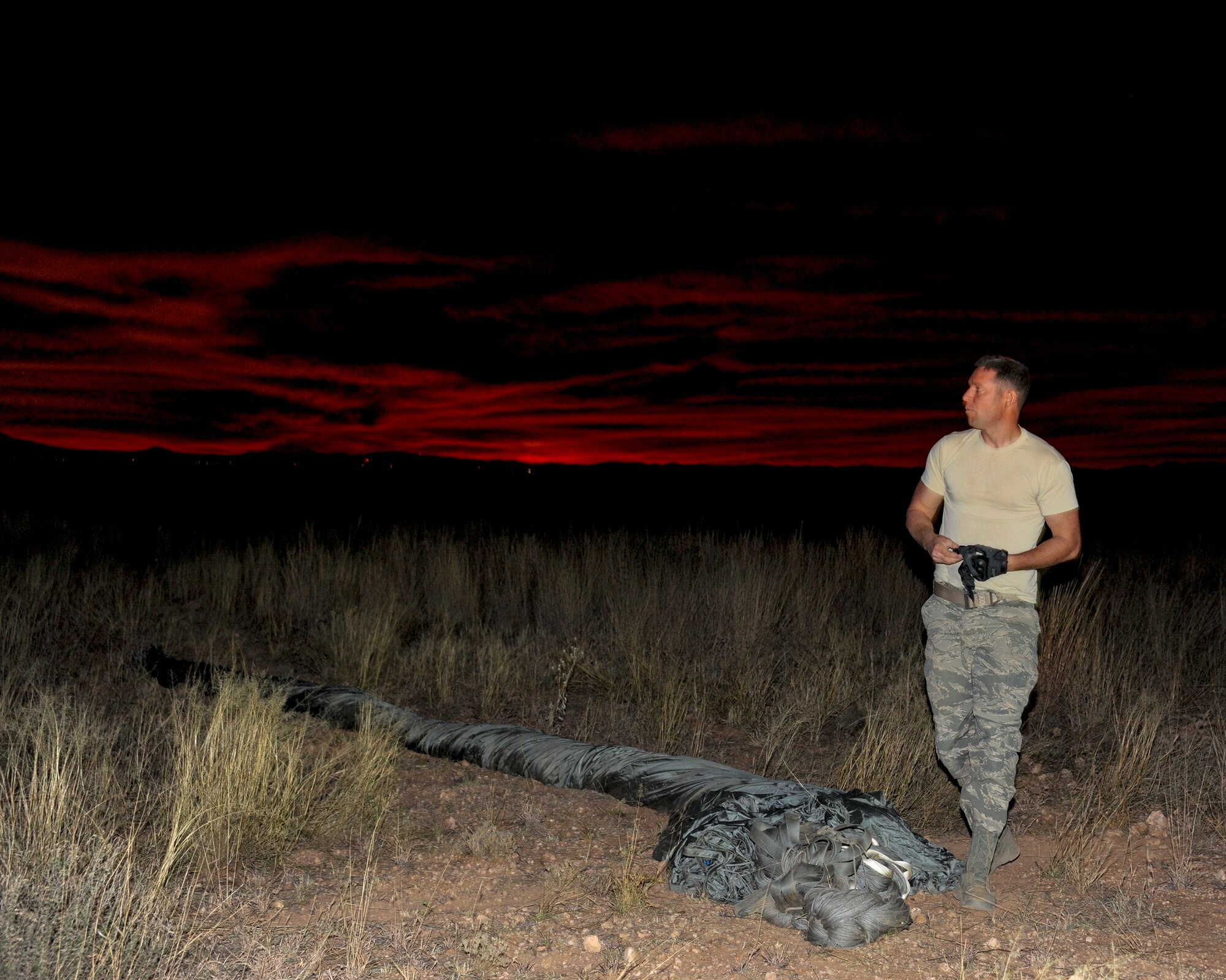 U.S. Air Force Staff Sgt. Mykal Sequeira, 563rd Operations Support Squadron aerial transportation craftsman, removes his gloves after rolling up a parachute during aerial delivery and recovery training at Fort Huachuca, Ariz., Dec. 9, 2015. This training marked the first time that any rescue operations support squadron packaged and rigged a heavy vehicle without external assistance and the first time a heavy vehicle was dropped by the 79th Rescue Squadron. (U.S. Air Force photo by Senior Airman Chris Massey/Released)