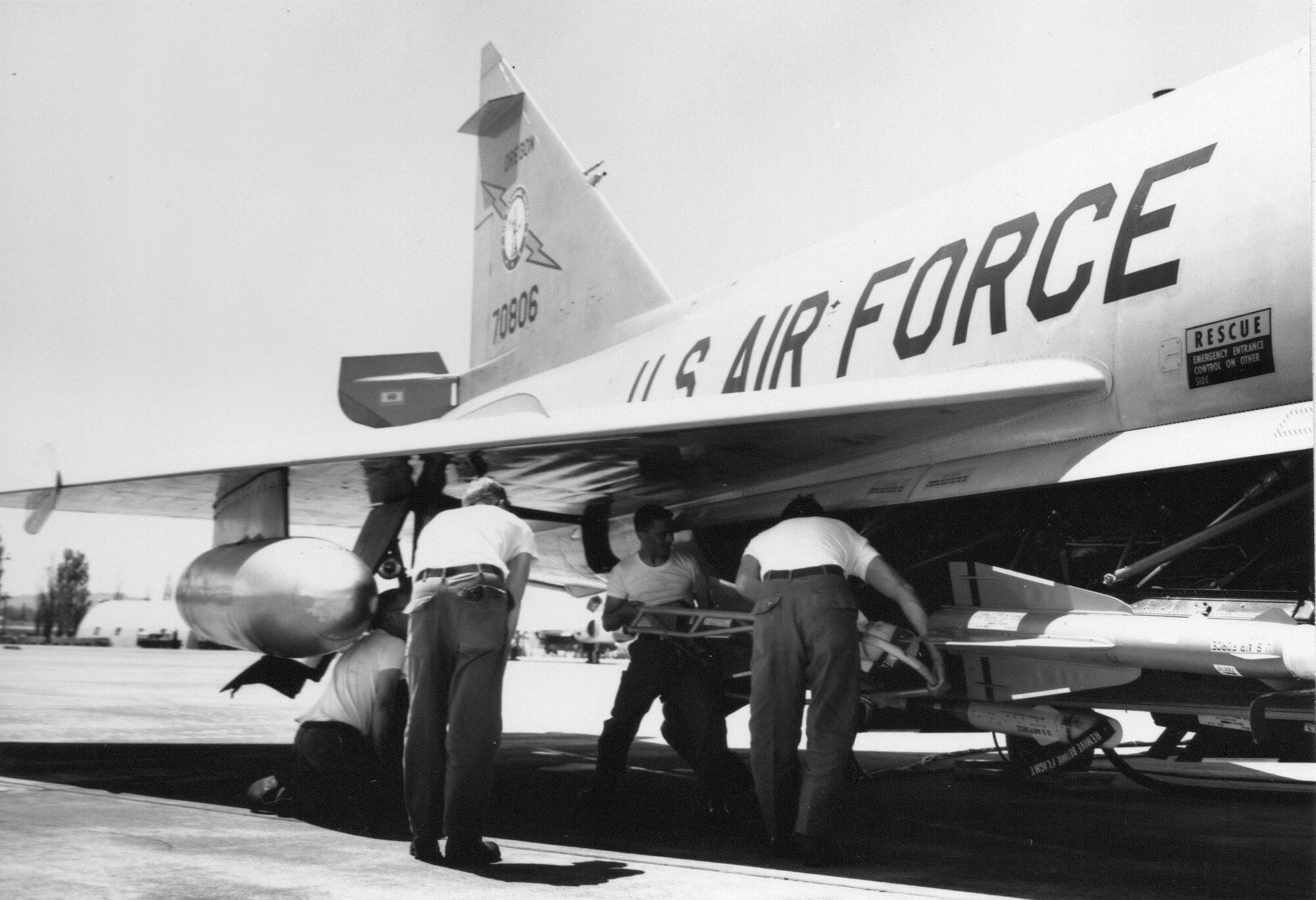 Two Oregon Air Guardsmen of a four-man Weapons load team lift an AIM-4 Falcon air-to-air missile in a cradle up into the missile bay of a F-102 Delta Dagger fighter-interceptor at Portland Air Base, Oregon, circa 1968.  OreANG Weapons troop Bill McAuley remembers “You almost had to be a contortionist to load the center rails.” The F-102 could carry six AIM-4 missiles in tandem pairs, left, center and right in the weapons bay.  (142nd Fighter Wing History Archives)