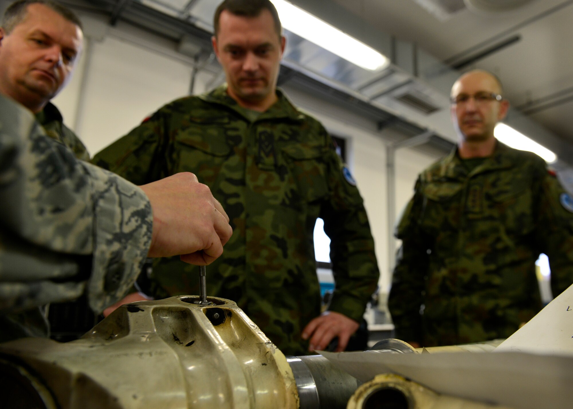 Polish air force members watch a U.S. Air Force Airman from the 31st Maintenance Squadron metals technology section measure an aircraft part during a joint training event, Dec. 15, 2015, at Aviano Air Base, Italy. The training afforded U.S. and Polish air force members the opportunity to better understand how they each maintain F-16 Fighting Falcon parts. (U.S. Air Force photo by Airman 1st Class Cary Smith/Released)