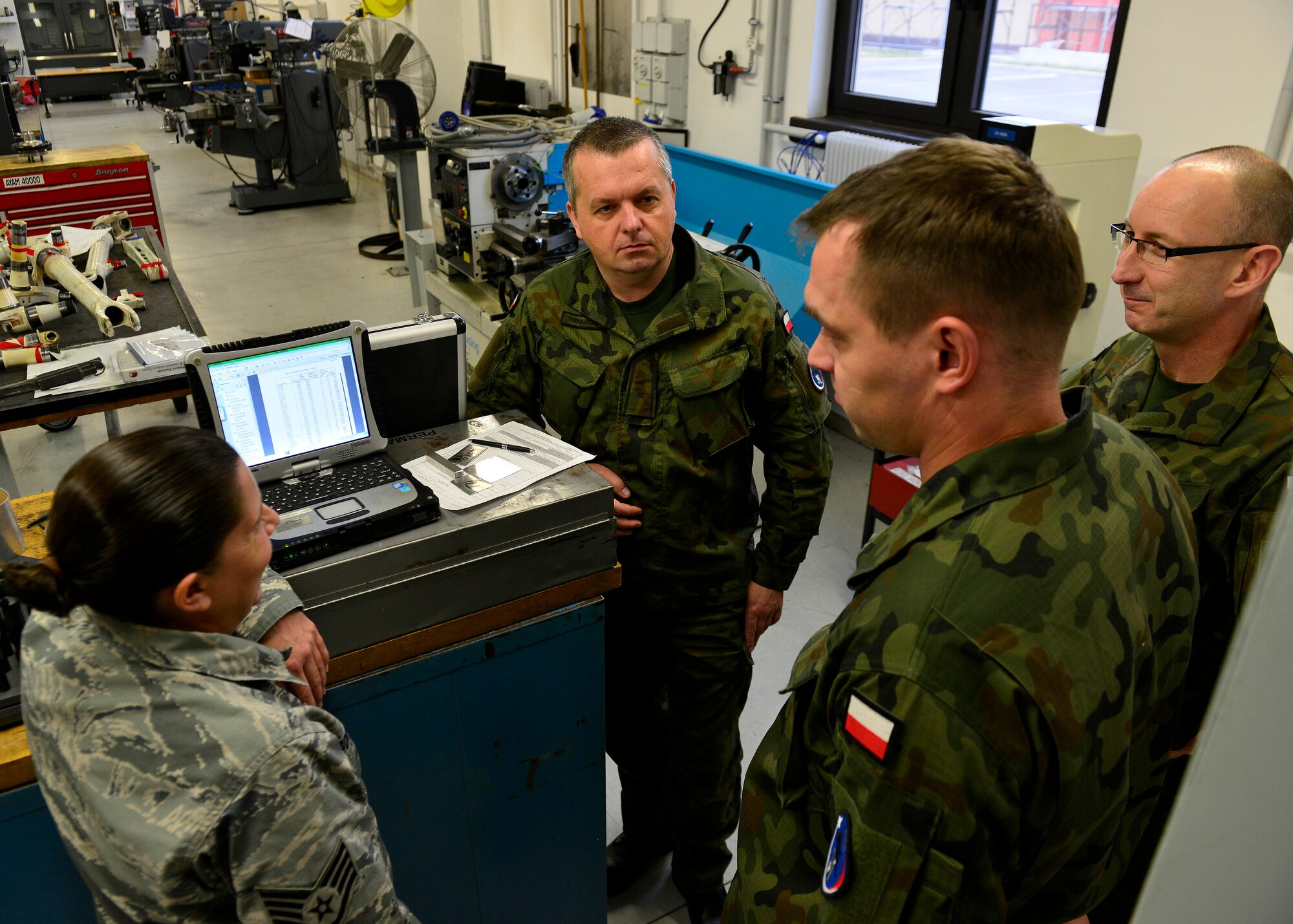 (From left) U.S. Air Force Staff Sgt. Lisa McDermott, 31st Maintenance Squadron aircraft metals technology craftsman, and Polish air force members discuss technical procedures during a joint training event, Dec. 15, 2015, at Aviano Air Base, Italy. The training included inspection procedures, heat stress tests and aircraft part measurements. (U.S. Air Force photo by Airman 1st Class Cary Smith/Released)