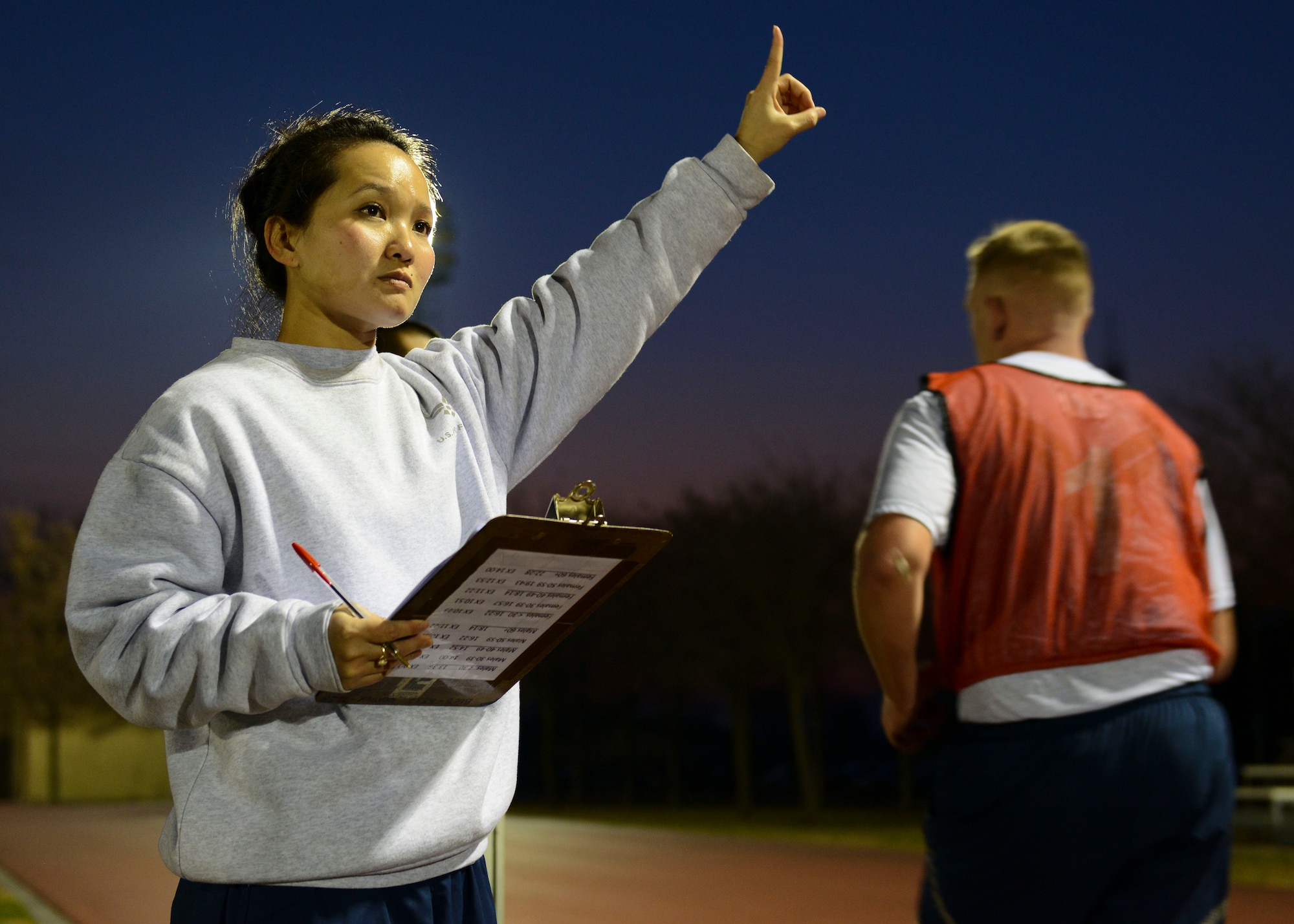 U.S. Air Force Staff Sgt. Ny Vu, 31st Comptroller Squadron unit fitness program manager, signals to a  fitness assessment participant that he has only one lap remaining, Dec. 14, 2015, at Aviano Air Base, Italy. The 31st Force Support Squadron Fitness Assessment Cell personnel conduct more than 400 FAs every month at Aviano and its eight geographically separated units. (U.S. Air Force photo by Senior Airman Austin Harvill/Released)