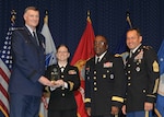 DLA director Air Force Lt. Gen. Andy Busch, left, presents Navy Lt. Jill Corrales, retail manager at Distribution Cherry Point, N.C., with the Company Grade Officer of the Year award at the 48th annual employee recognition ceremony Dec. 10.  Distribution’s commander Army Brig. Gen. Richard Dix, second from right, and DLA’s Senior Enlisted Leader Army Command Sgt. Maj. Charles Tobin, right, were also on-hand to present the award.