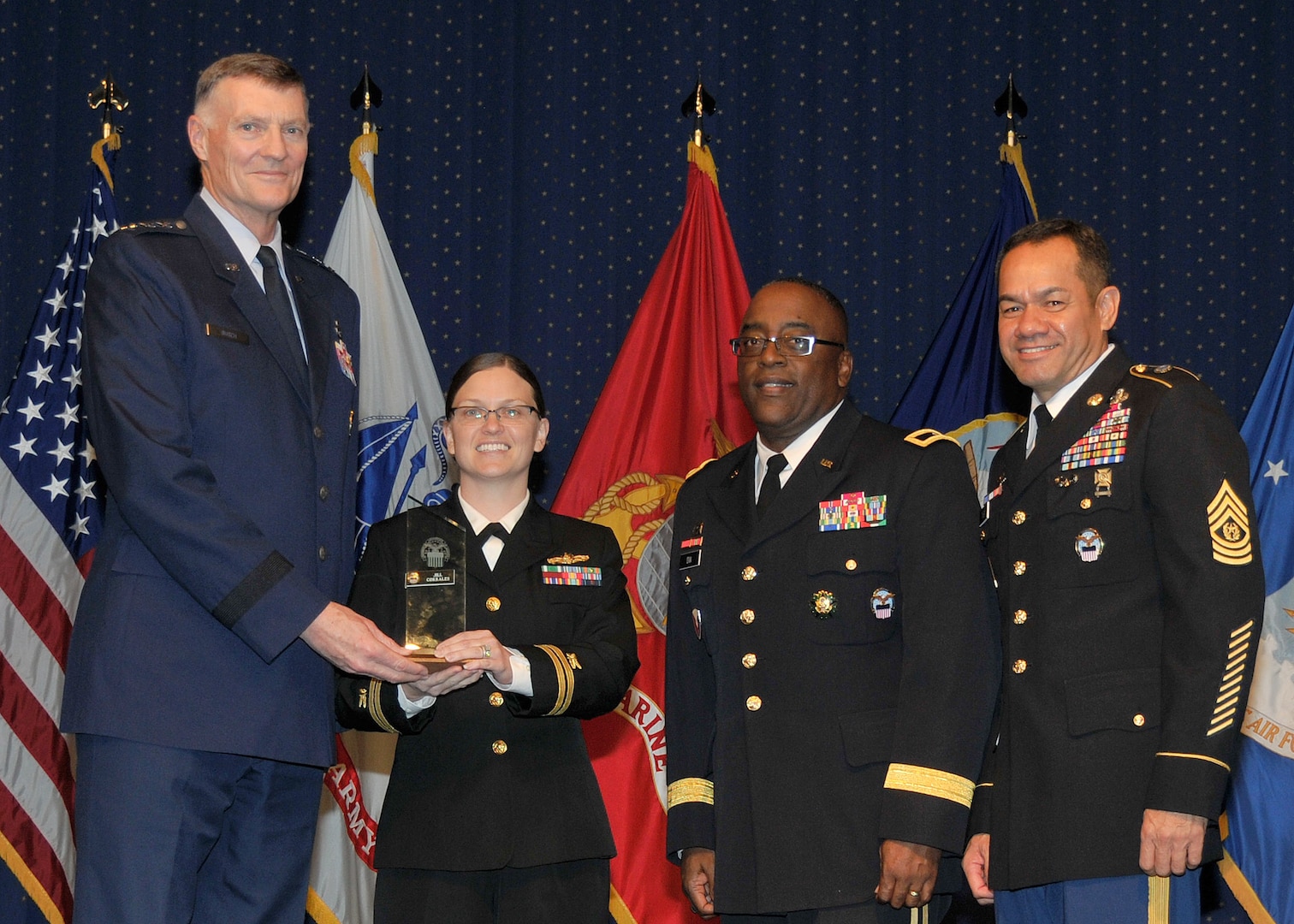 DLA director Air Force Lt. Gen. Andy Busch, left, presents Navy Lt. Jill Corrales, retail manager at Distribution Cherry Point, N.C., with the Company Grade Officer of the Year award at the 48th annual employee recognition ceremony Dec. 10.  Distribution’s commander Army Brig. Gen. Richard Dix, second from right, and DLA’s Senior Enlisted Leader Army Command Sgt. Maj. Charles Tobin, right, were also on-hand to present the award.