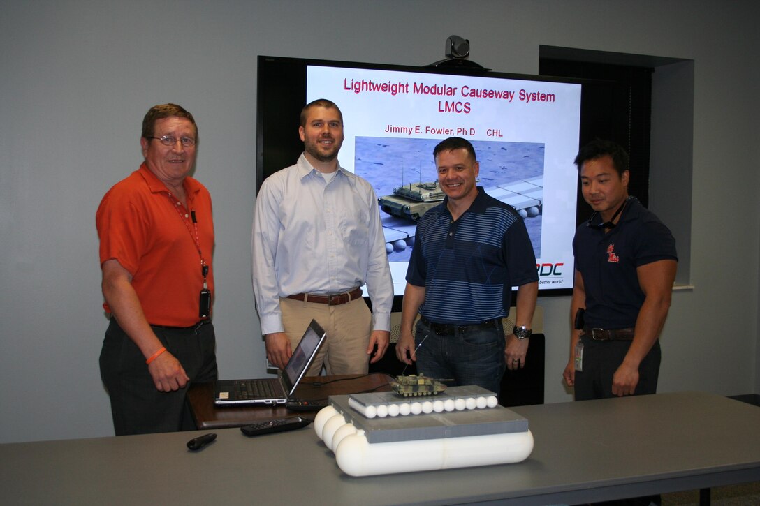 Dr. Jimmy Fowler and Dr. Mark Wahl  explaining the table model and briefing the Lightweight Modular Causeway System (LMCS) to MAJ Wallace Mattos, the Military Personnel Exchange Program Officer.  Also shown is Bo Tennant, Security.  MAJ Mattos was  learning about the program to support his upcoming mission representing ERDC in Brazil.