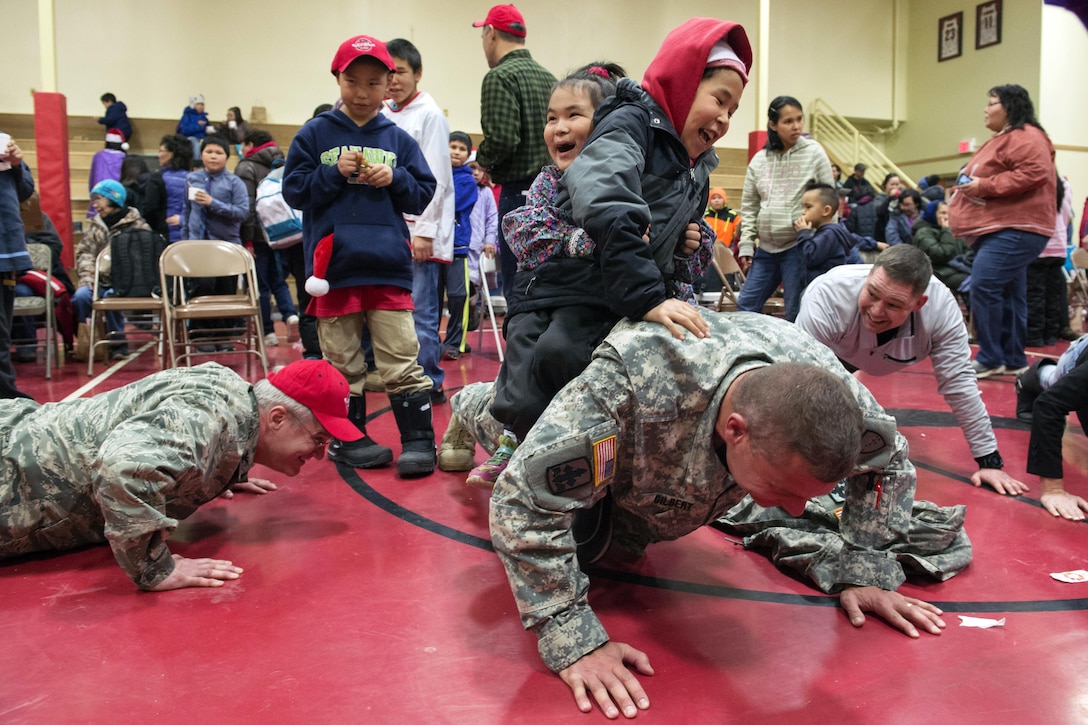 Alaska Army National Guard Lt. Col. Joel Gilbert, right, does pushups with school students on his back at St. Mary's, Alaska, during Operation Santa Claus, Dec. 5, 2015. U.S. Air Force photo by Alejandro Pena
