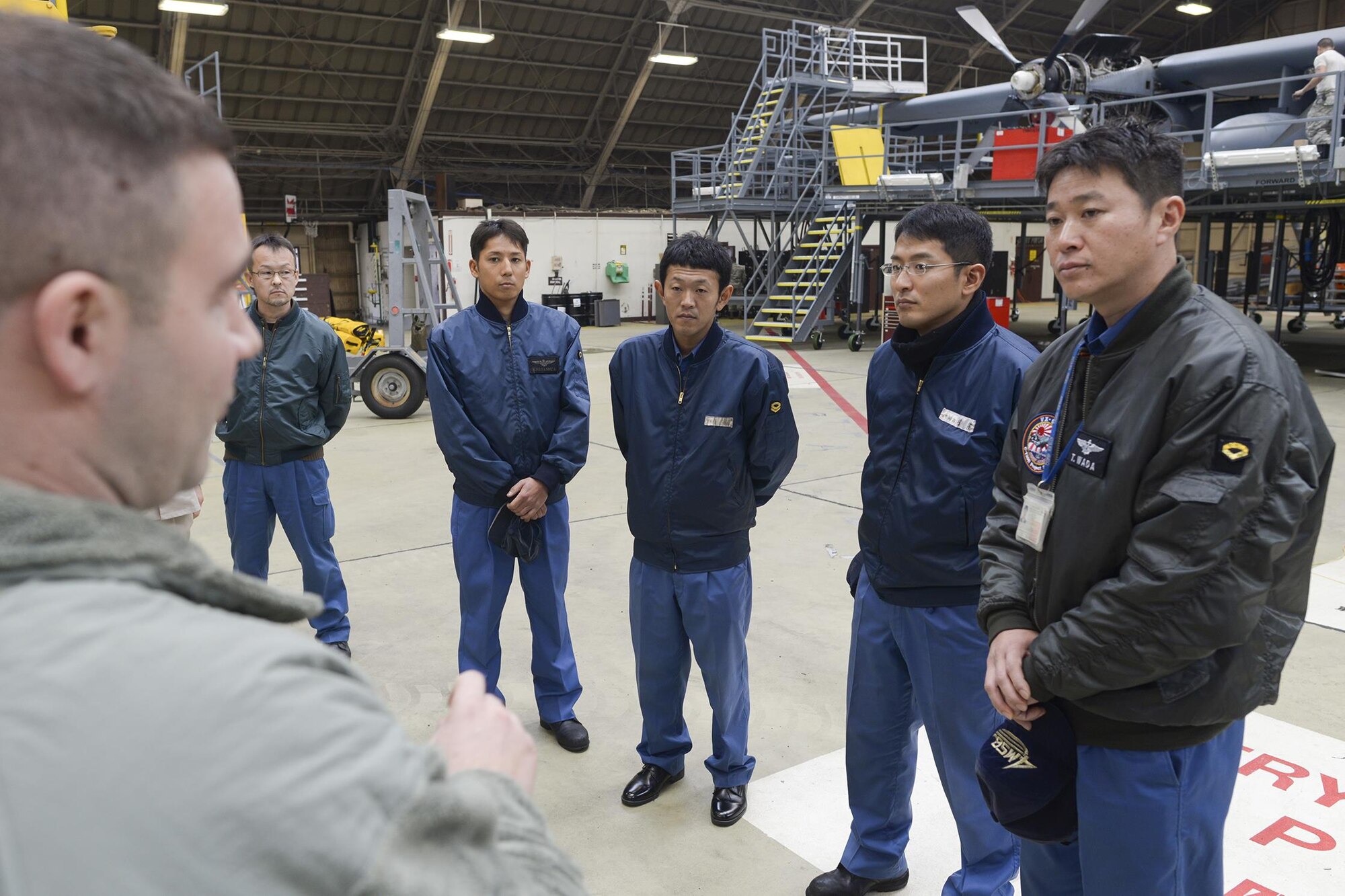 Japan Maritime Self-Defense Force members with the 4 Maintenance Squadron listen to Master Sgt. Aaron Ross, 374th Maintenance Squadron isochronal inspection dock chief, during a facility tour at Yokota Air Base, Japan, Dec. 11, 2015. Nine JMSDF members visited Yokota to learn about C-130 Hercules maintenance conducted at Yokota. (U.S. Air Force photo by Staff Sgt. Cody H. Ramirez/Released)