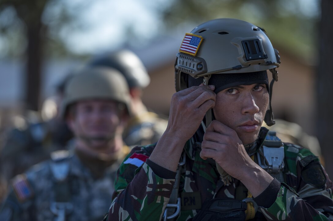 Indonesian Lt. Dwinanda Noryanzha, foreground, son of Indonesian Defence Minister Ryamizard Ryacudu, adjusts a strap on an advanced combat helmet before performing a static line jump during the Randy Oler Memorial Operation Toy Drop on Camp Mackall, N.C., Dec. 8, 2015. 