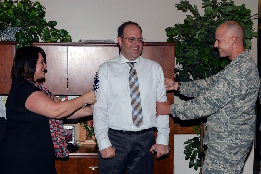 U.S. Air Force Col. Joseph Locke, (right), 93d Air Ground Operations Wing commander, and Kristin Olszewski, 93d AGOW secretary, tack on her husband, Senior Master Sgt. Jason Olszewski, 93d AGOW wing intel and inspector general superintendent, after receiving notification he was selected for chief master sergeant,  Dec. 17, 2015, at Moody Air Force Base, Ga. The rank of chief master sergeant was created after the authorization of the Military Pay Act of 1958. (U.S. Air Force photo by Airman 1st Class Janiqua P. Robinson/Released)