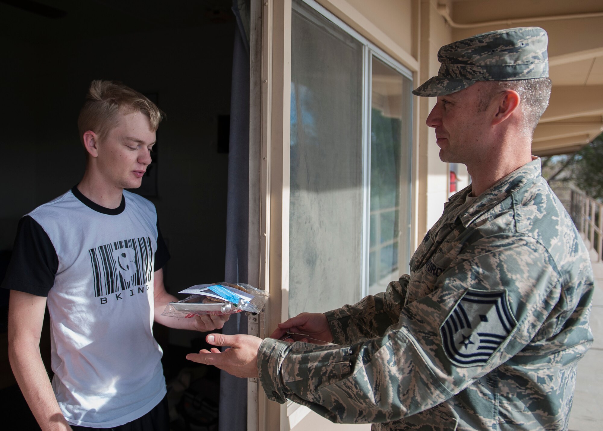 Airman 1st Class Bradley Greer, 99th Security Forces Squadron member, receives a cookie package from Senior Master Sgt. Christopher McEwan, 99th SFS first sergeant, during the Airman Cookie Drive at Nellis Air Force Base, Nev., Dec. 14, 2015. McEwan and other first sergeants delivered more than 12,000 cookies to Airmen living in the Nellis AFB dormitories. (U.S. Air Force photo by Staff Sgt. Siuta B. Ika)