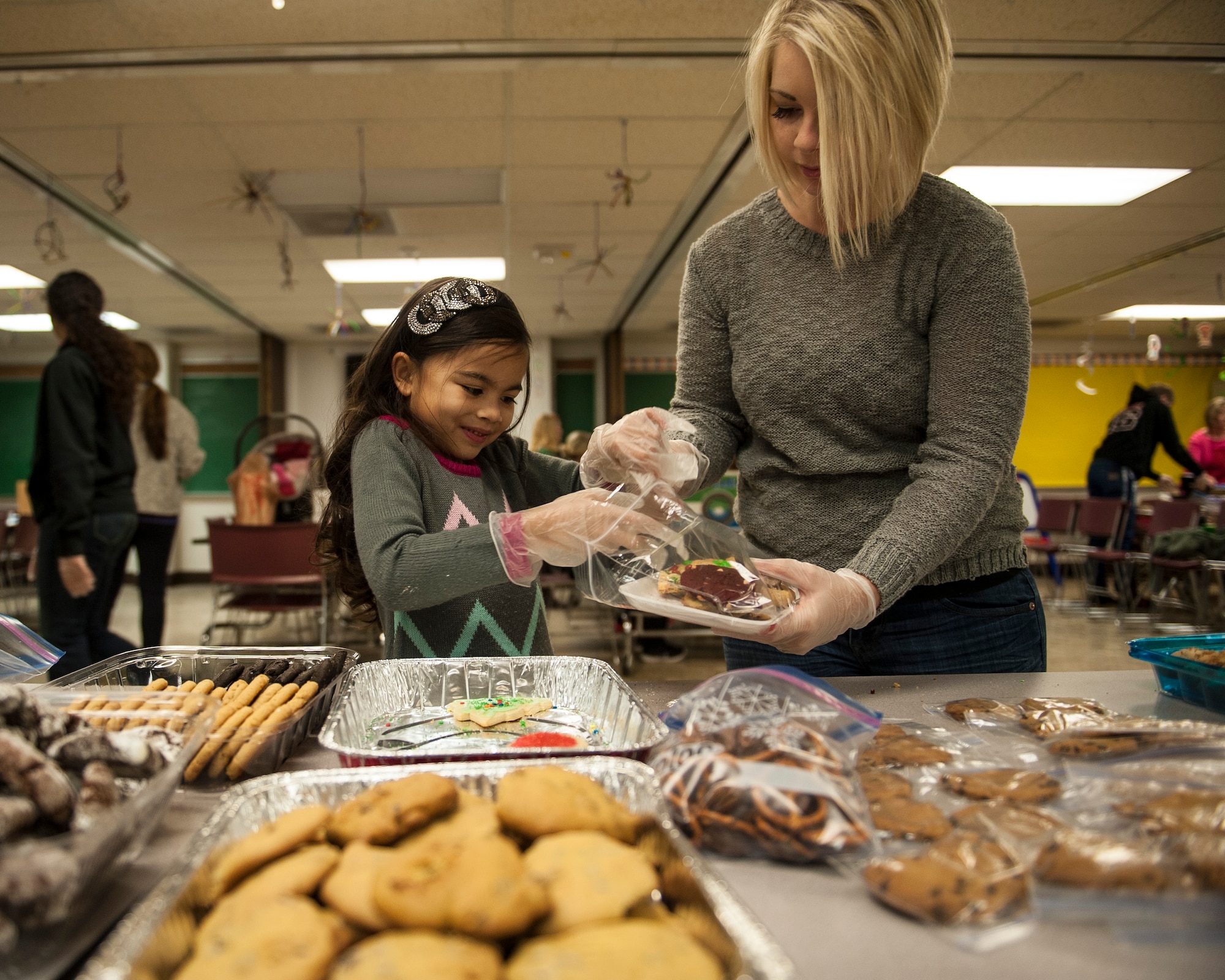 Kalena, 8, helps her mother put cookies onto a tray during the Airman Cookie Drive at Nellis Air Force Base, Nev., Dec. 14, 2015. Kalena was one of approximetly 100 volunteers who came together to show Airmen living in the Nellis AFB dormitories they are not forgotten during the holiday season. (U.S. Air Force photo by Staff Sgt. Siuta B. Ika)