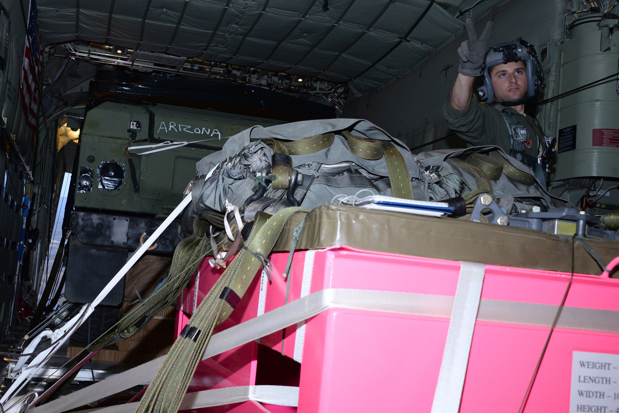 U.S. Air Force Staff Sgt. Russell Bickel, 79th Rescue Squadron loadmaster, signals two minutes until extraction to the aircrew in a HC-130J Combat King II during aerial delivery and recovery training with the 563rd Operations Support Squadron while flying over Fort Huachuca, Ariz., Dec. 9, 2015. The HC-130J aircrew completed two airdrops weighing approximately 12,780 pounds. (U.S. Air Force photo by Airman 1st Class Mya M. Crosby/Released)