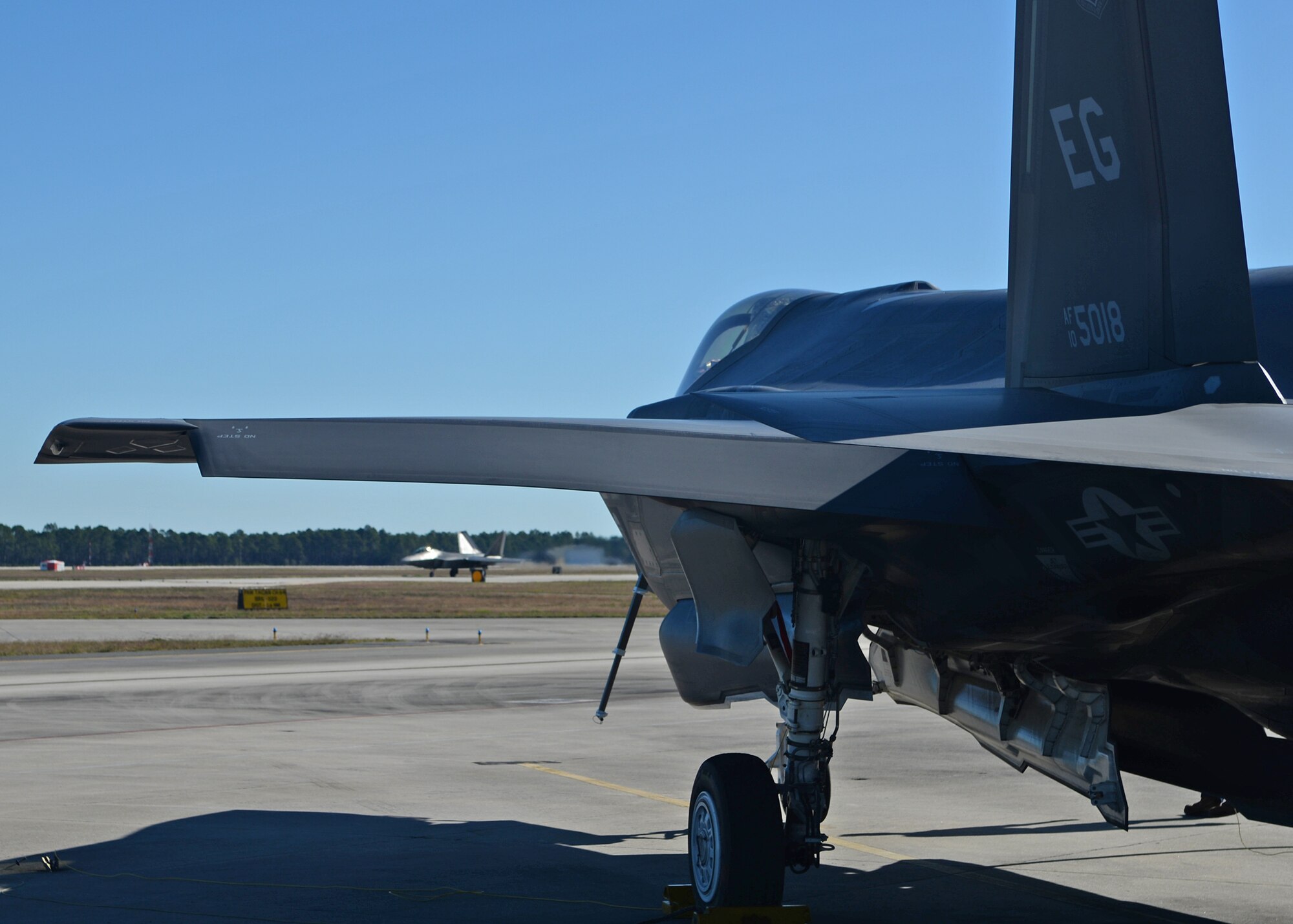 An Eglin Air Force Base, Fla., F-35 Lightning II sits on the Tyndall AFB, Fla., flightline Dec. 15 as an F-22 Raptor launches from the runway during the Checkered Flag 16-1 exercise. During this large-force exercise, fourth and fifth generation aircraft integrated their capabilities to provide better situational awareness for the Air Force fleet. (U.S. Air Force photo by Senior Airman Sergio A. Gamboa/Released) 
