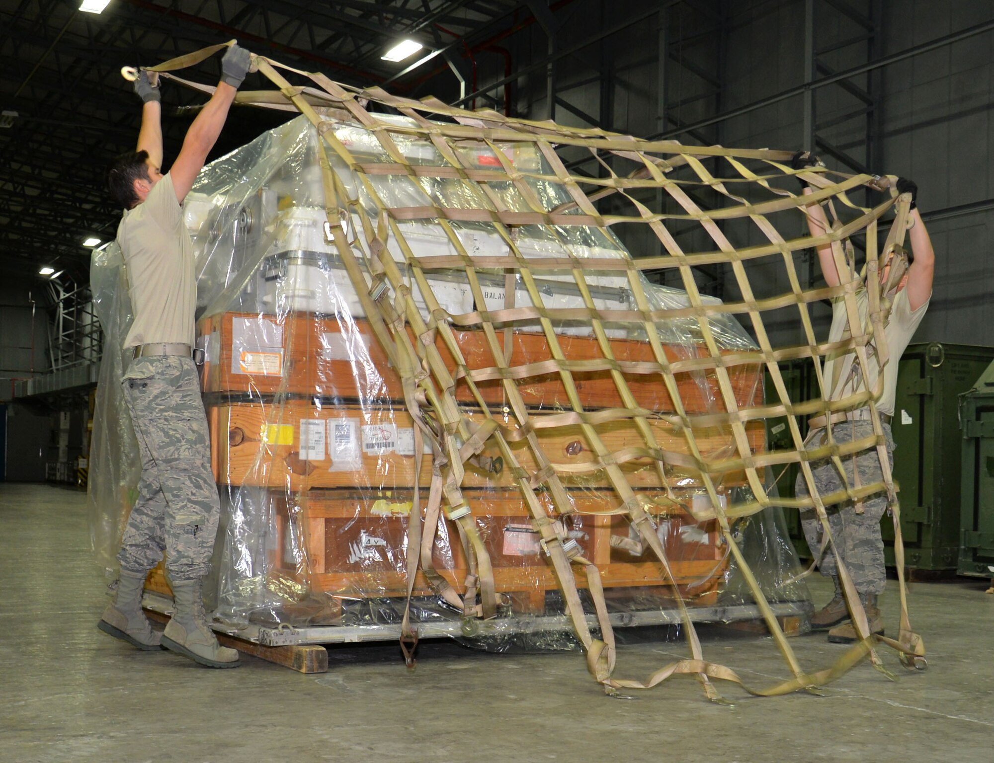 U.S. Air Force Senior Airman Juan Gavidia, left, and U.S. Air Force Senior Airman Marcus Anguiano, right, both 100th Logistics Readiness Squadron Mobility Readiness Spares Packages technicians, secure a cargo net to a pallet load Dec. 10, 2015, on RAF Mildenhall, England. The net keeps the cargo stable during transit to reduce the risk of damage as a result of movement. (U.S. Air Force photo by Gina Randall/Released)