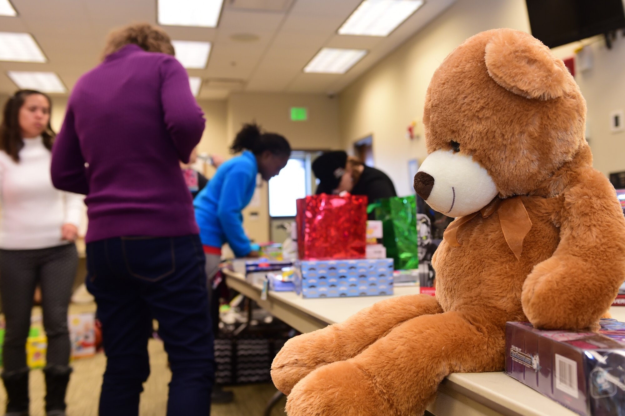 A teddy bear awaits a new home while volunteers prepare gifts Dec. 17, 2015, at the chapel on Buckley Air Force Base, Colo. The Buckley Spouses Group gathered all the donations from the Angel Tree in order to ready them for distribution. (U.S. Air Force photo by Airman 1st Class Luke W. Nowakowski/Released)