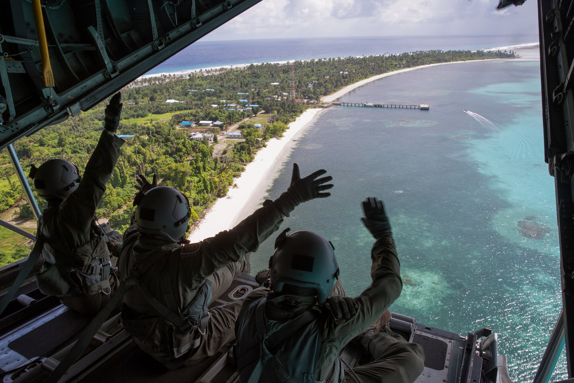 Airmen from Team Yokota and Andersen wave out the back of a C-130H Hercules to the people of Kayangel, Republic of Palau, Dec. 11, 2015, during Operation Christmas Drop. Every December, C-130H Hercules aircrews from Yokota head to Andersen Air Force Base to execute low-cost, low-altitude humanitarian airdrops to islanders throughout the Commonwealth of the Northern Marianas, Federated States of Micronesia, Republic of Palau. These islands are some of the most remote locations on the globe spanning a distance nearly as broad as the continental U.S. It is the longest-running Department of Defense humanitarian airdrop operation with 2015 being the first trilateral execution with support from Japan Air Self-Defense Force and Royal Australian Air Force. (U.S. Air Force photo by Osakabe Yasuo/Released)