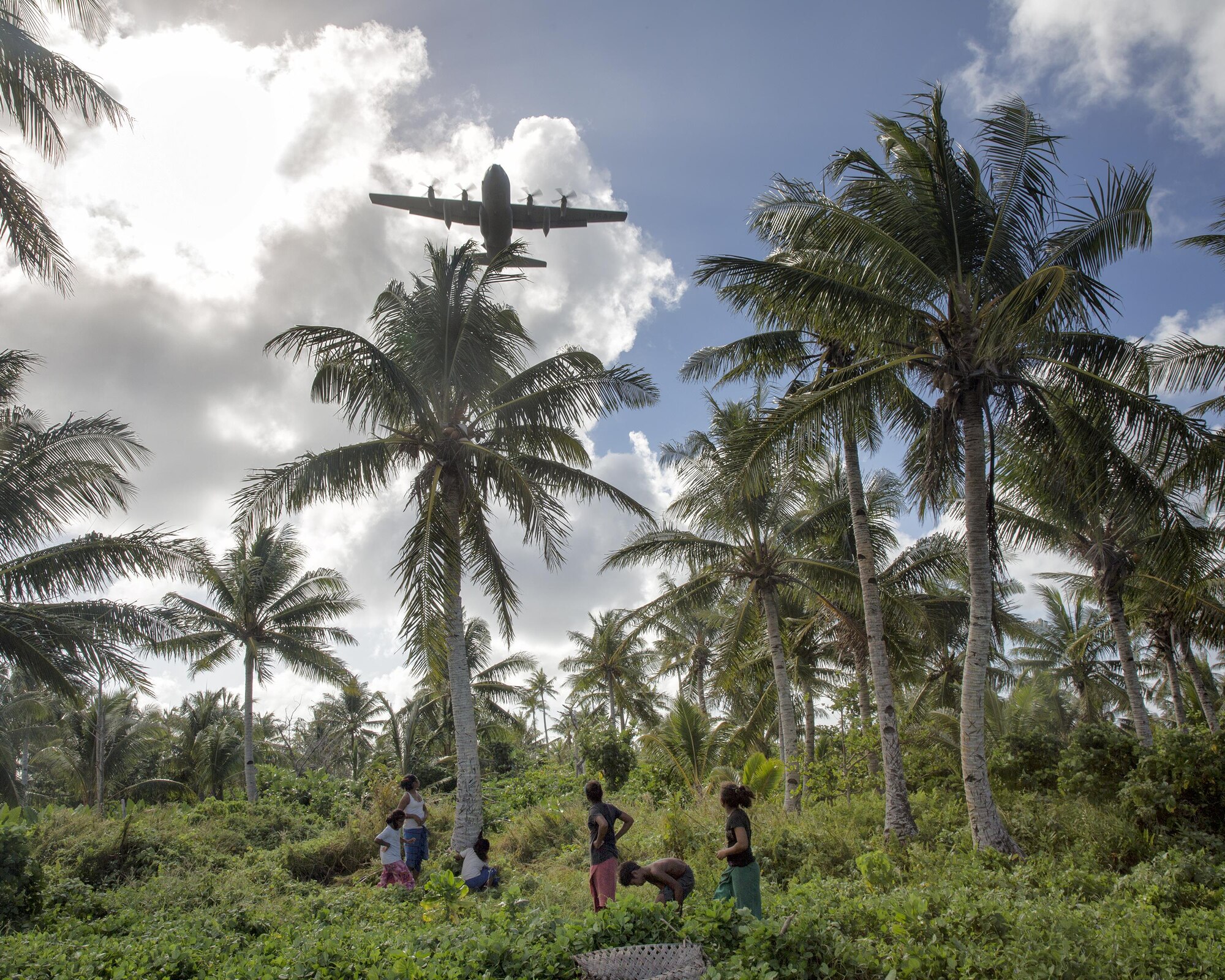 Islanders from Fais watch a C-130 Hercules fly over head during Operation Christmas Drop 2015, at Fais island, Federated States of Micronesia, Dec. 8, 2015. A C-130 Hercules assigned to the 36th Airlift Squadron delivered over 800 pounds of supplies to the island of Fais during Operation Christmas Drop 2015. This year marks the first ever trilateral Operation Christmas Drop where the U.S. Air Force, Japan Air Self-Defense Force and the Royal Australian Air Force work together to provide critical supplies to 56 Micronesian islands.(U.S. Air Force photo by Osakabe Yasuo/Released)
