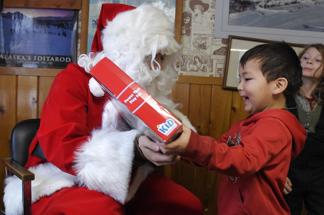Marine Corps Sgt. Mauricio Sandoval, left, playing Santa Claus, passes out toys to children during Toys for Tots at Takotna, Alaska, Dec. 10, 2015. Sandoval is assigned to Delta Company, 4th Law Enforcement Battalion. U.S. Air Force photo by Alejandro Pena