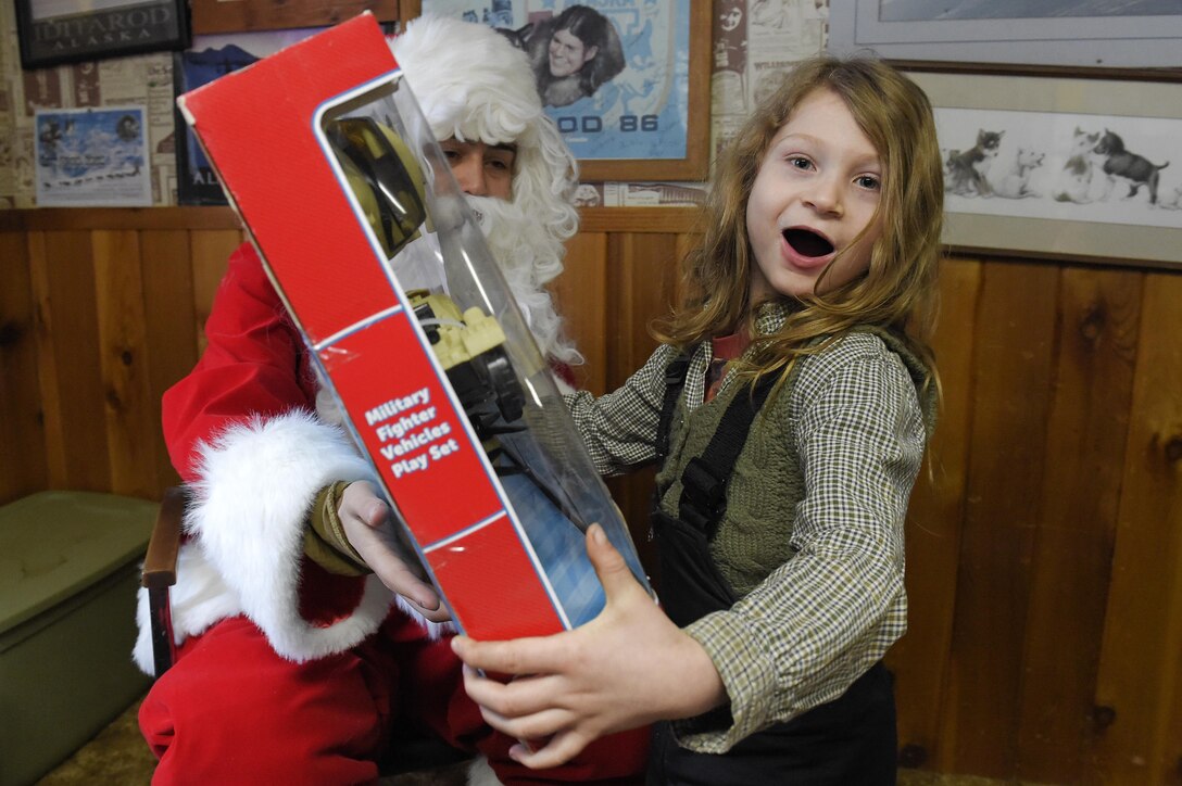 Marine Corps Sgt. Mauricio Sandoval, left, playing Santa Claus, gives a toy to a girl during Toys for Tots at Takotna, Alaska, Dec. 10, 2015. Sandoval is assigned to Delta Company, 4th Law Enforcement Battalion. U.S. Air Force photo by Alejandro Pena