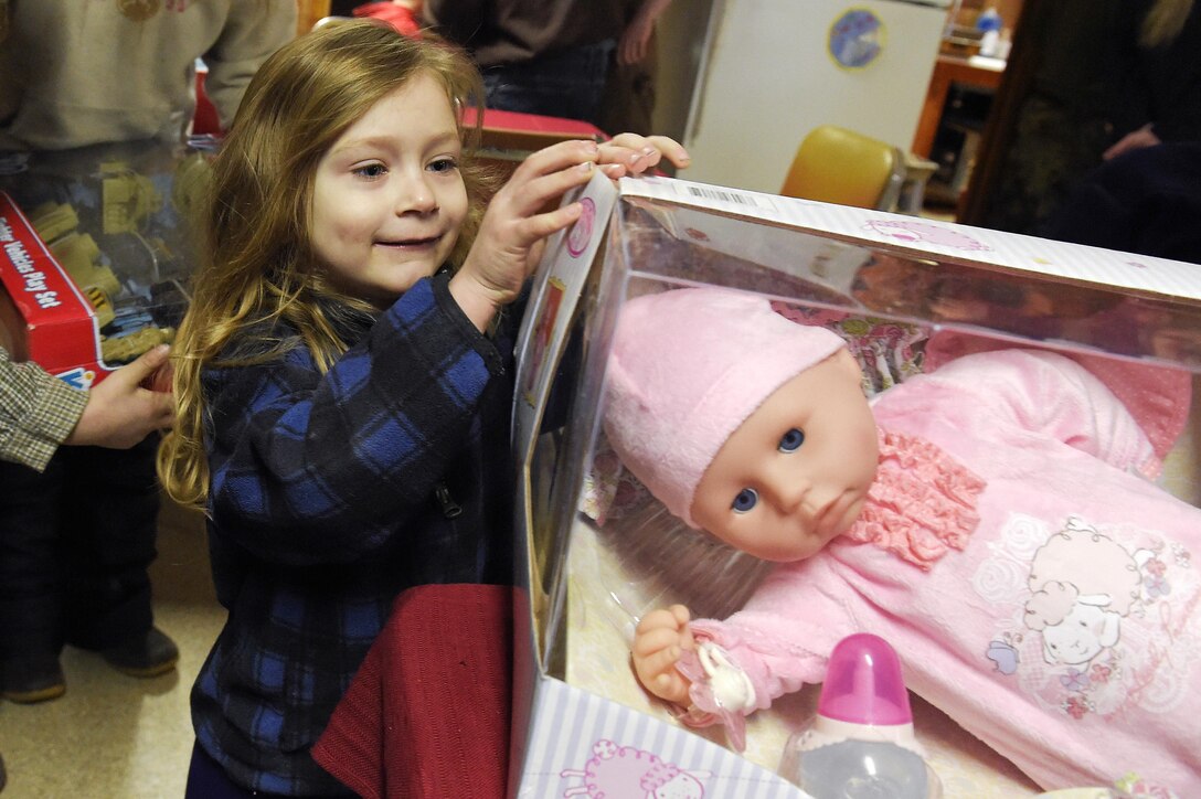 Lea Dopler, 3, looks at her new doll brought by Santa Claus, played by Marine Corps Sgt. Mauricio Sandoval, not shown, during Toys for Tots in Takotna, Alaska, Dec. 10, 2015. U.S. Air Force photo by Alejandro Pena