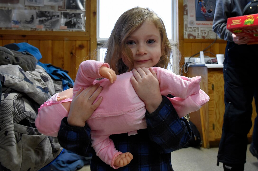 Lea Dopler, 3, stops for a photo while embracing her new doll brought by Santa Claus, played by Marine Corps Sgt. Mauricio Sandoval, not shown, during Toys for Tots in Takotna, Alaska, Dec. 10, 2015. U.S. Air Force photo by Alejandro Pena