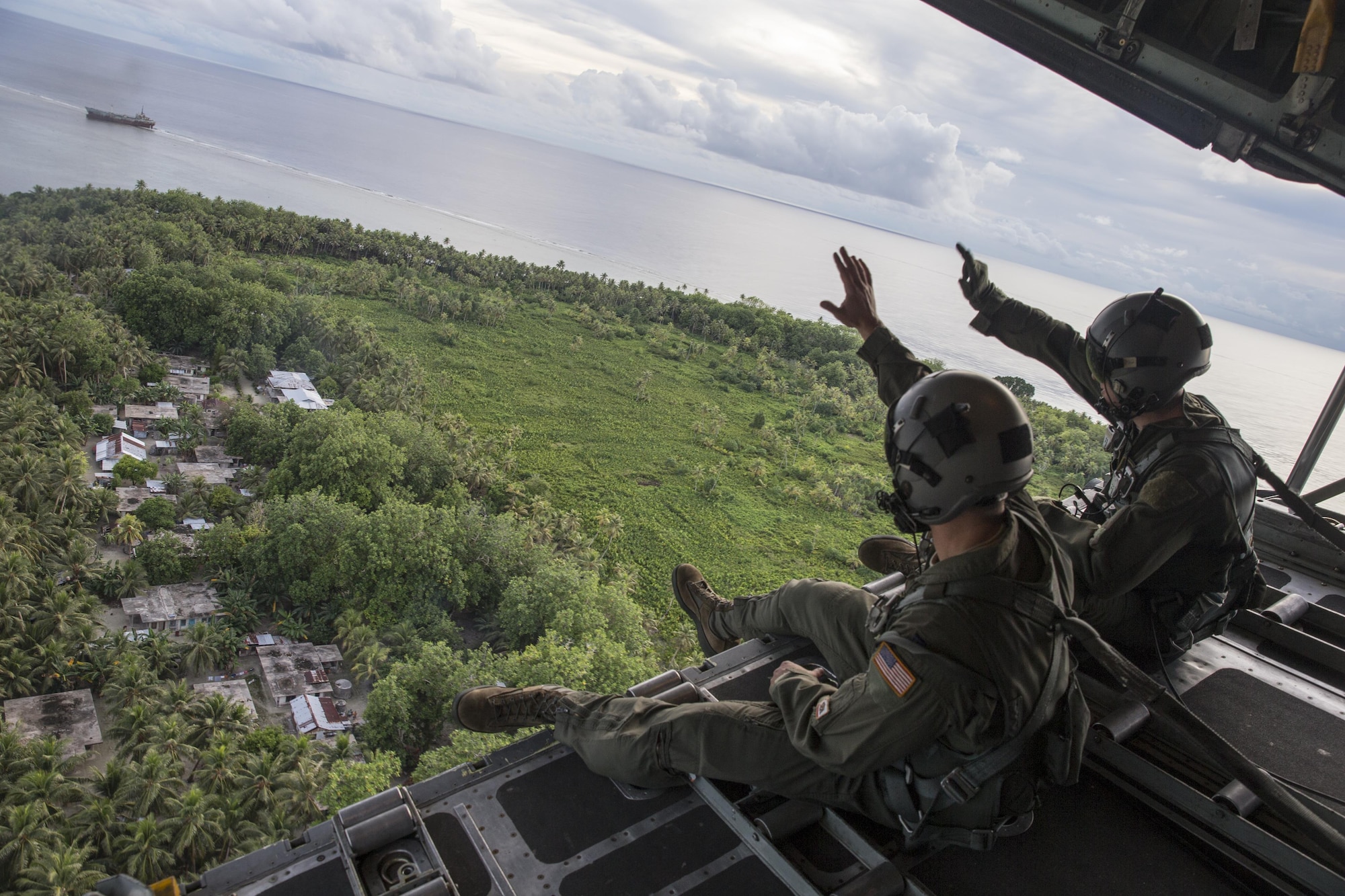(Right to left) Staff Sgt. Ren Forbes and Airman 1st Class Alexander Lauher, 36th Airlift Squadron loadmasters, wave out the back of a C-130H Hercules to the people of the Namoluk Island, Federated States of Micronesia, Dec. 9, 2015, during Operation Christmas Drop. Every December, C-130H Hercules aircrews from Yokota head to Andersen Air Force Base to execute low-cost, low-altitude humanitarian airdrops to islanders throughout the Commonwealth of the Northern Marianas, Federated States of Micronesia, Republic of Palau. These islands are some of the most remote locations on the globe spanning a distance nearly as broad as the continental U.S. It is the longest-running Department of Defense humanitarian airdrop operation with 2015 being the first trilateral execution with support from Japan Air Self-Defense Force and Royal Australian Air Force. (U.S. Air Force photo by Osakabe Yasuo/Released)