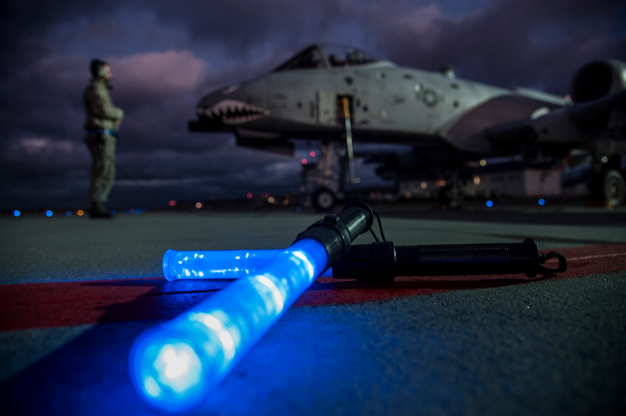 A pair of marshaling light wands sit on the flightline while U.S. Air Force Airman 1st Class Tony Nagel, 74th Expeditionary Fighter Squadron crew chief, communicates with Capt. Matt Mecadon, 74th EFS A-10 Thunderbolt II attack aircraft pilot, during pre-flight inspections on the flightline, Nov. 11, 2015, at Amari Air Base, Estonia.  The light wands assist in marshaling aircraft in low-light scenarios. (U.S. Air Force photo by Andrea Jenkins/Released)