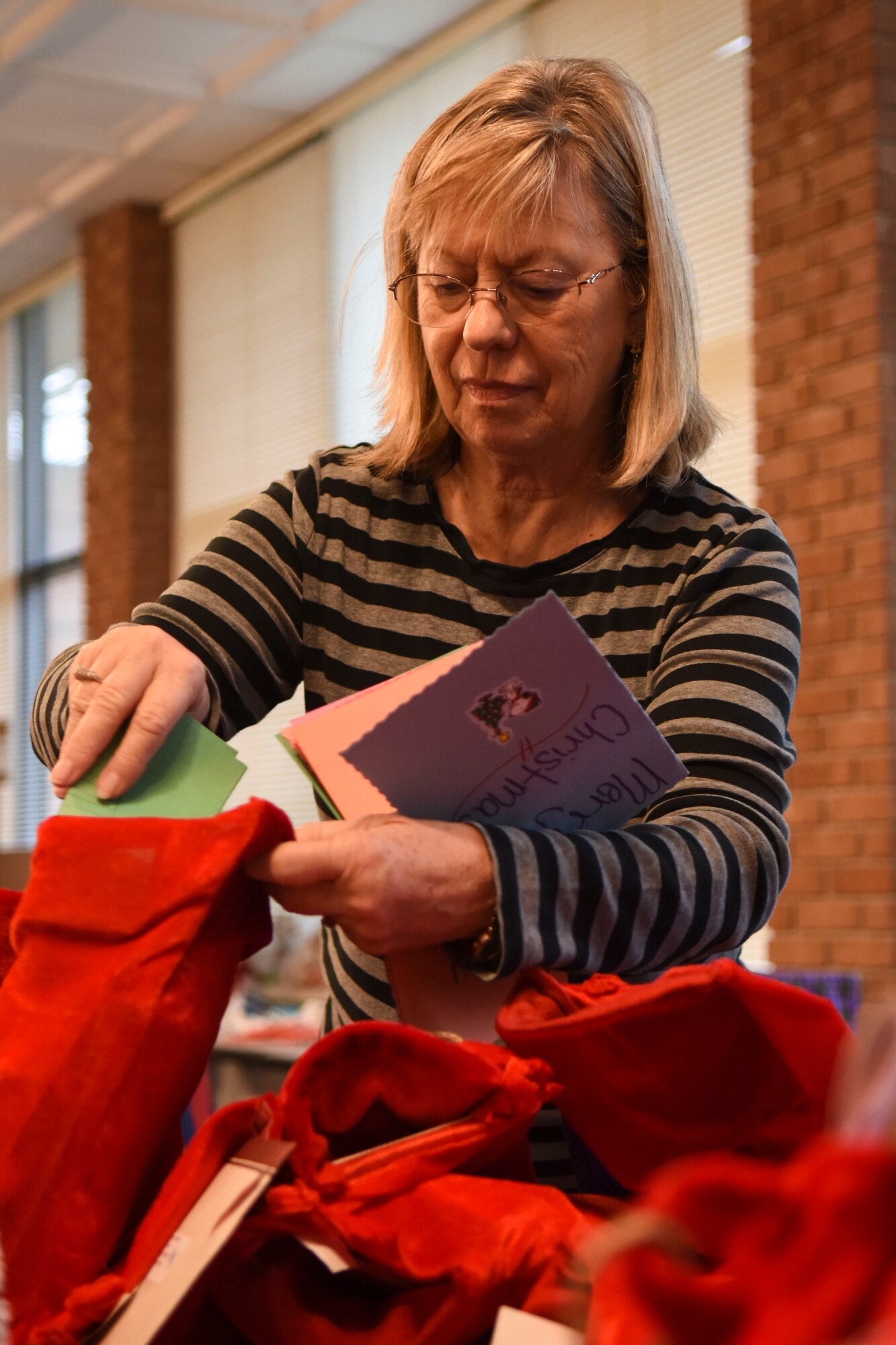 Jan Raecher, 4th Fighter Wing Chapel volunteer, places holiday cards in stockings, Dec. 17, 2015, at Seymour Johnson Air Force Base, North Carolina. Stockings were filled with items such as razors, candy, and snack items, donated by the chapel and community members, and delivered to Airmen living in the dorms. (U.S. Air Force photo/Airman Shawna L. Keyes)