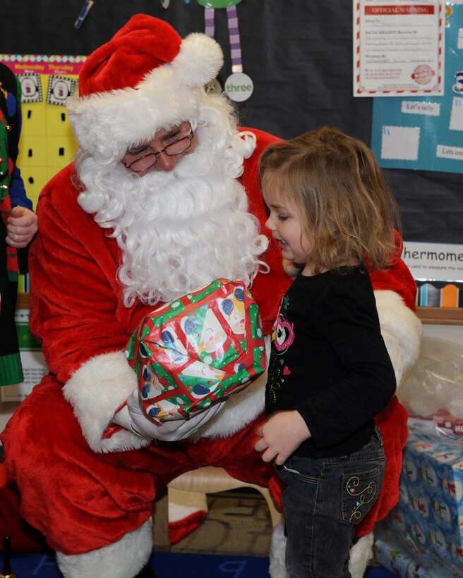 Santa hands a child her Christmas present during the annual Angel Tree program at the Youth and Family Services Center in Rapid City, S.D., Dec. 17, 2015.More than 200 gifts were provided for the children enrolled in the YFS Child Care program. (U.S. Air Force photo by Airman 1st Class Denise M. Nevins/Released)