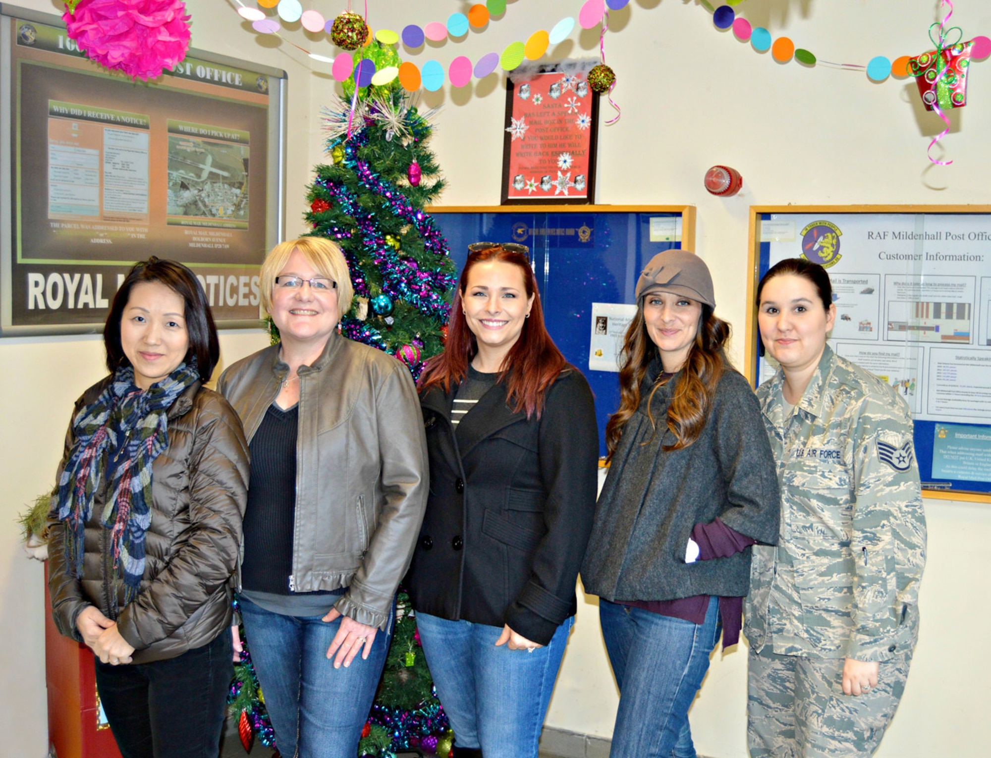 RAF Mildenhall spouses from left to right, Junko Schell, Charlotte Mauk, Kelly Ford and Lori Prater, along with U.S. Air Force Staff Sgt. Gloria Jolly, 100th Communications Squadron quality assurance evaluator, pose in front of a Christmas tree at the post office recently on RAF Mildenhall, England. The four spouses and Jolly worked as a team with spouse Jeannie Comley, and U.S. Air Force Staff Sgt. Alexandria Rader, 100th CS commander’s support staff NCO in charge, to decorate the base post office with a variety of themes to spread holiday cheer to Team Mildenhall’s Airmen and families. (Courtesy photo)