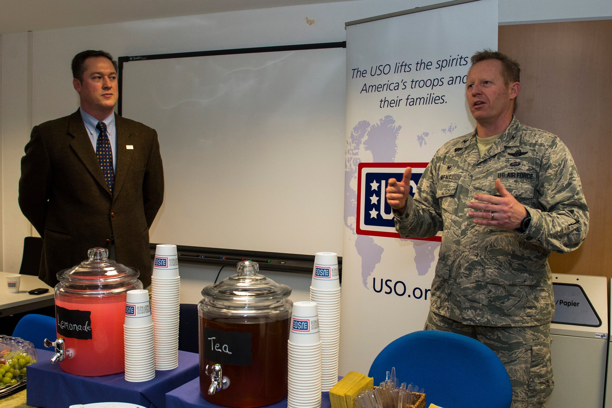 Konrad Braun, USO area director, left, listens as U.S. Air Force Col. Joe McFall, 52nd Fighter Wing commander, speaks to community members before a ribbon-cutting ceremony to officially open the USO at Spangdahlem Air Base, Germany, Dec. 16, 2015. McFall and U.S. Air Force Chief Master Sgt. Brian Gates, 52 FW command chief, coined Braun for leading the effort to complete the USO. The USO is located on the first floor of building 126. (U.S. Air Force photo by Airman 1st Class Luke Kitterman/Released)