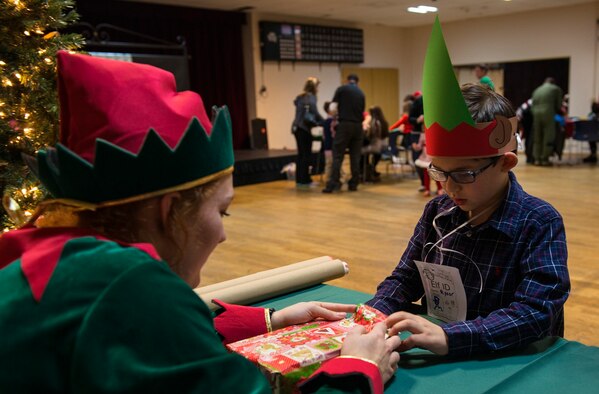 Zania Sterling, Ramstein Community Center volunteer, helps a child wrap a gift at the Elf Boot Camp Dec. 14, 2015, at Ramstein Air Base, Germany. The children at the event participated in multiple activities to see if they had the qualities to be an elf at the North Pole. Activities for Elf Boot Camp included creating an elf identification badge, making elf hats and taste-testing cookies. (U.S. Air Force photo/Airman 1st Class Tryphena Mayhugh)