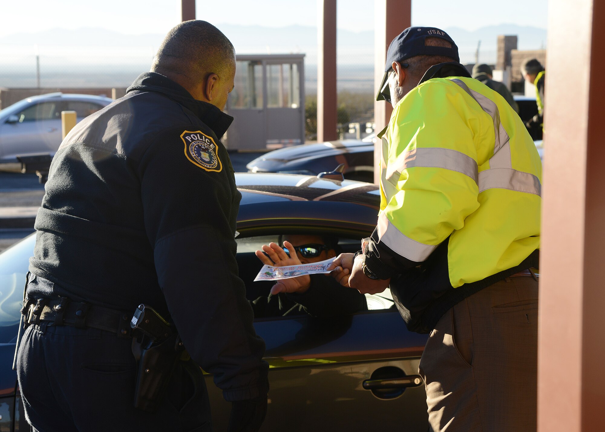 Murray Westley, 412th Civil Engineering Squadron director, handed out holiday pamphlets to each driver entering the West Gate while Officer Arbra Anthony checked their identification. (U.S. Air Force photo by Rebecca Amber)